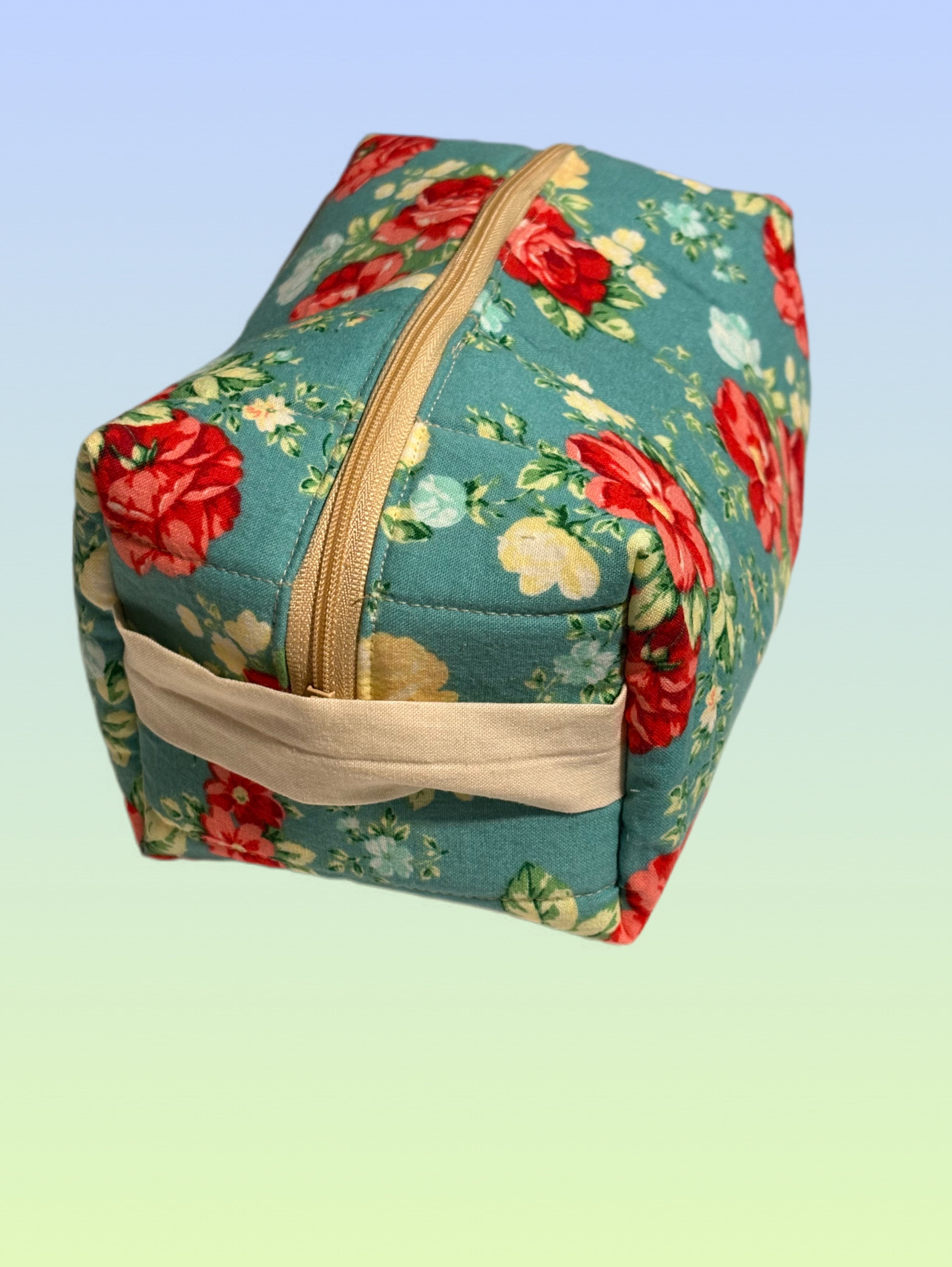 Handmade teal floral boxy bag with cream zipper and side handle, designed as a makeup or toiletry pouch.