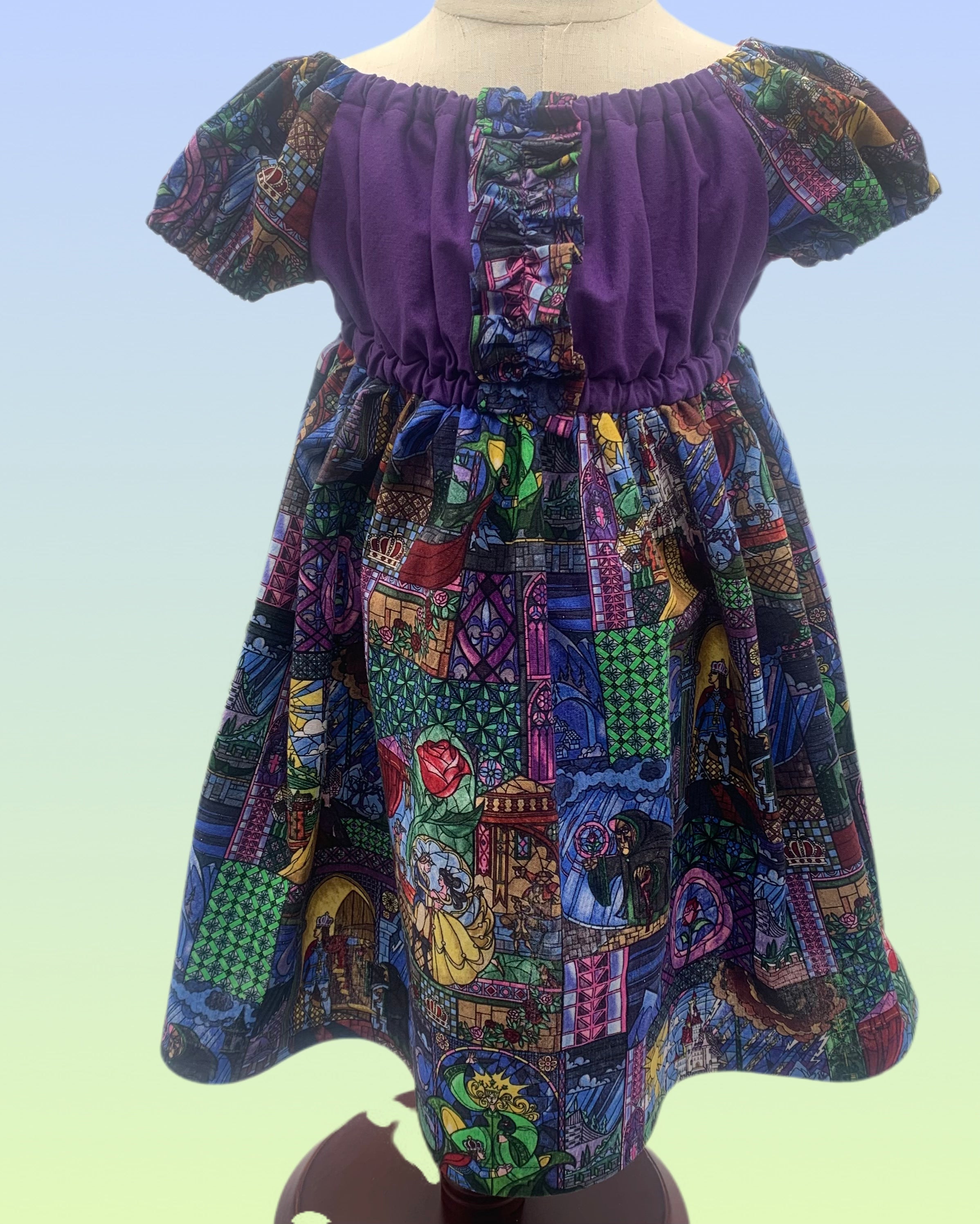 Handmade girls dress with purple bodice, gathered neckline, and colorful storybook print skirt with puff sleeves.