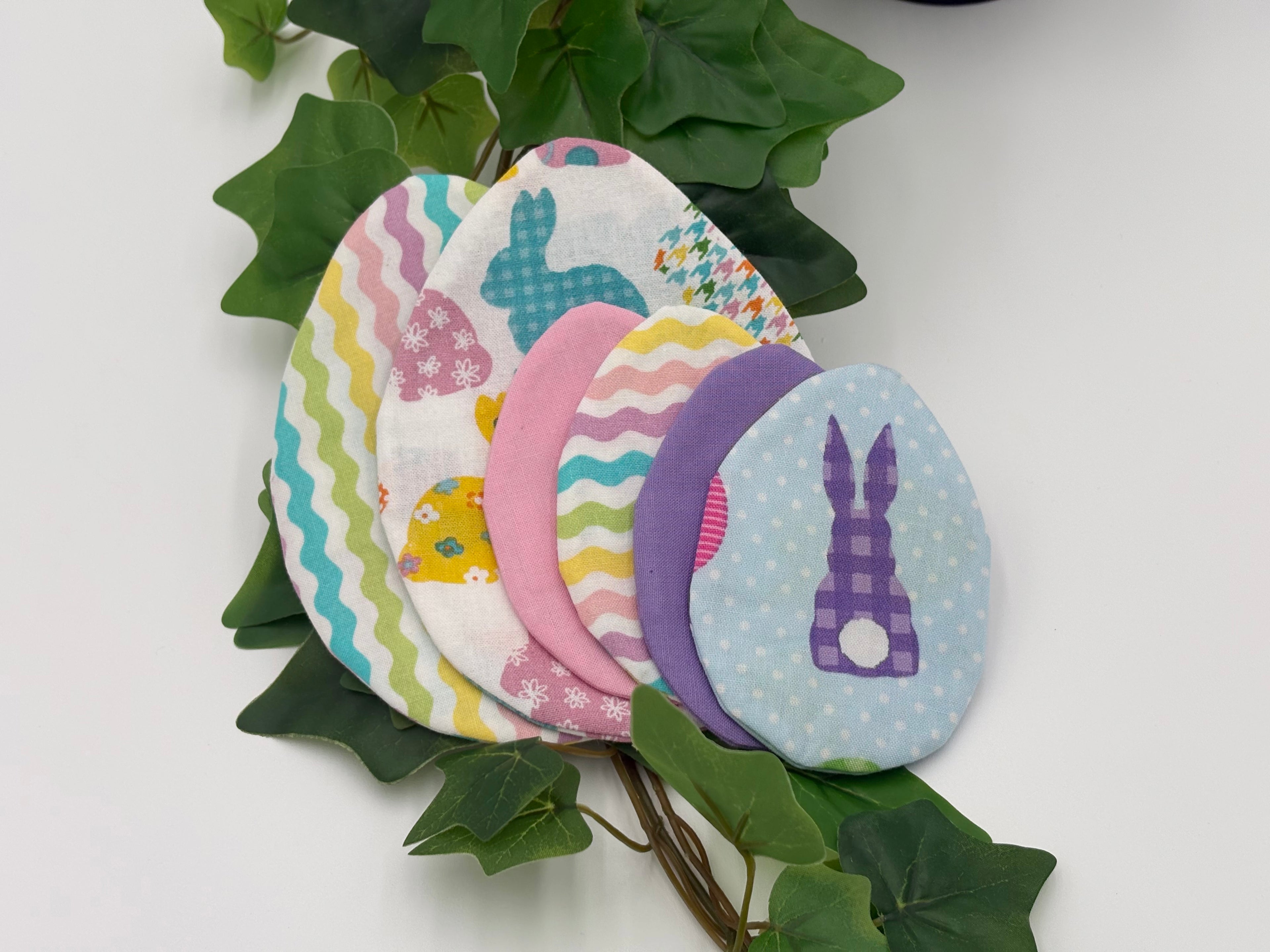 Colorful fabric Easter egg fillers on a white background with green leaves.