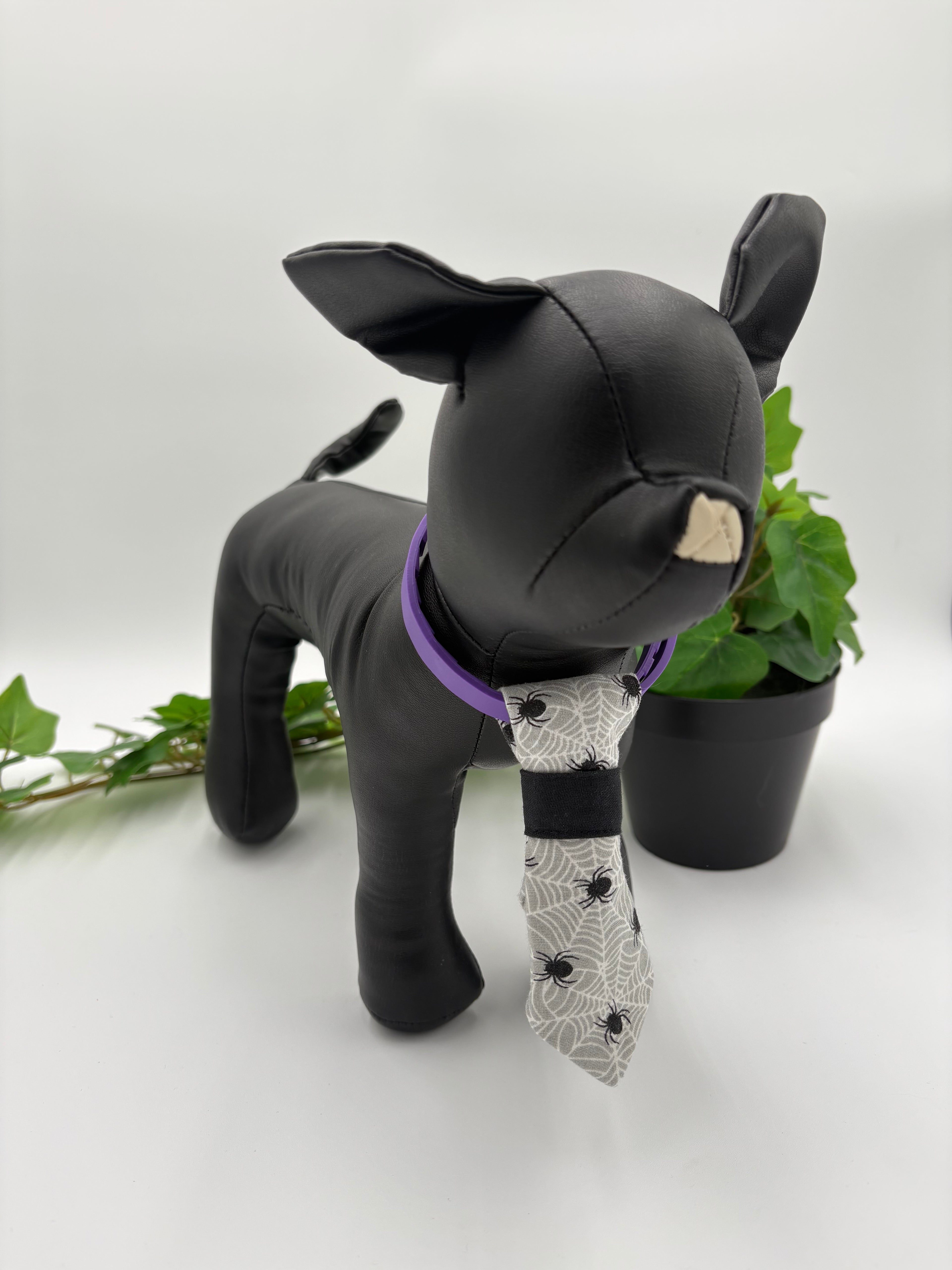 Black dog mannequin with a spiderweb necktie on a white background with green potted plant