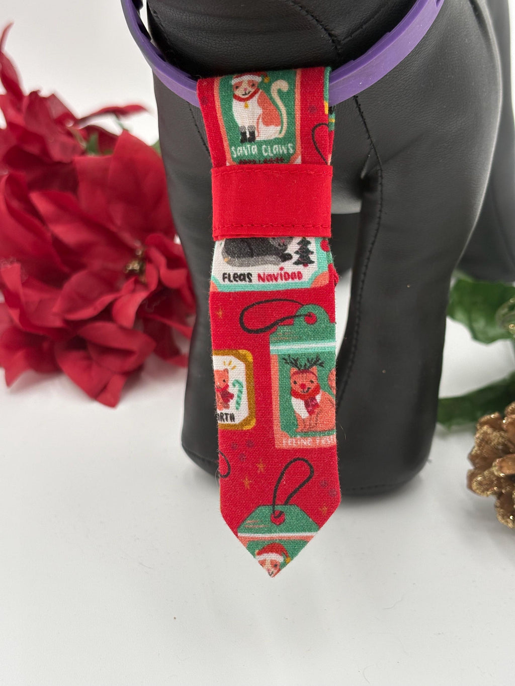 close up of Black dog mannequin standing with a Red Christmas-themed over the collar necktie with festive designs on a white background with poinsettias and a pine cone.