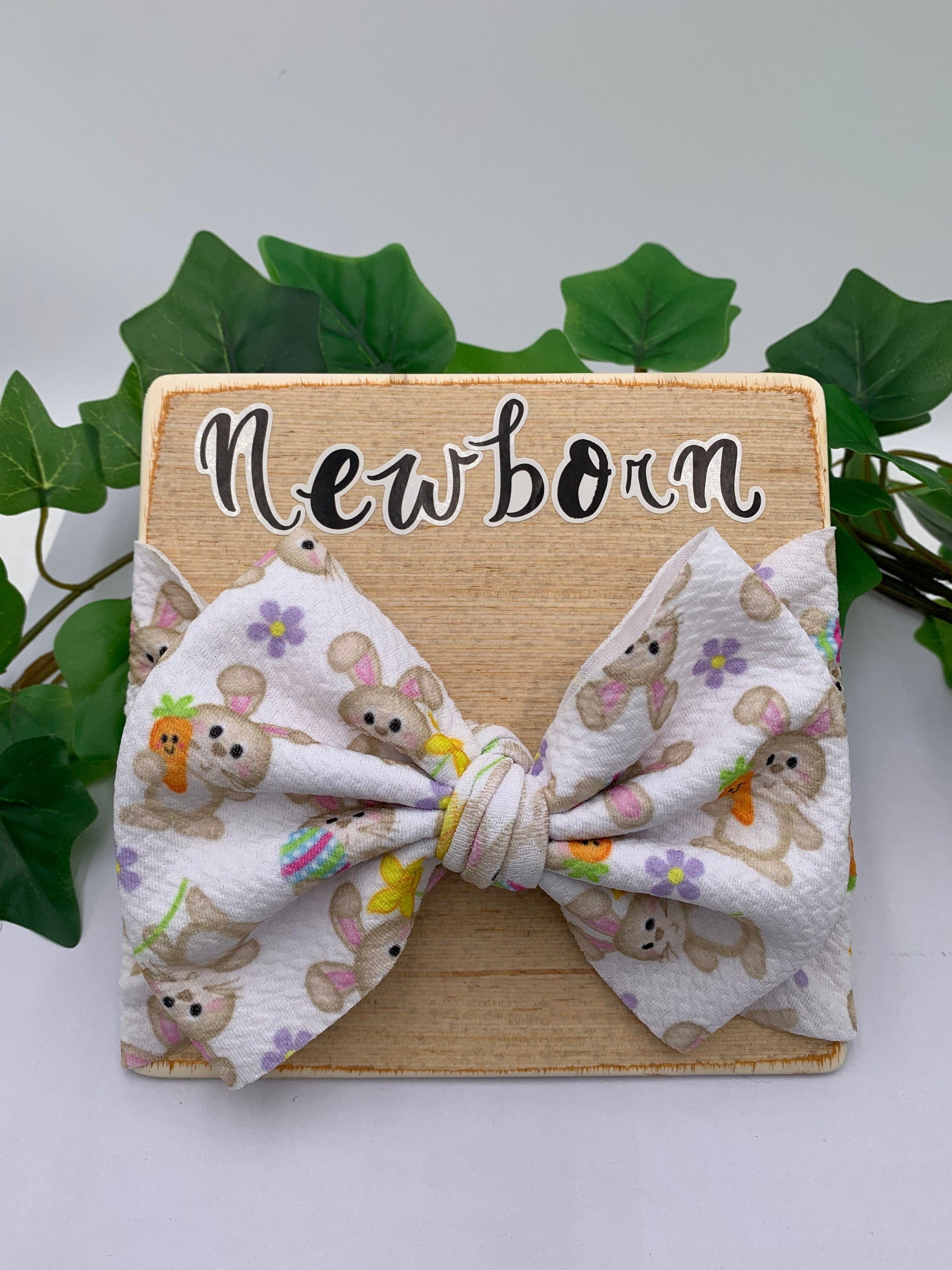 White Headband with a decorative bunny holding a carrot themed big bow on a wood board against a white background