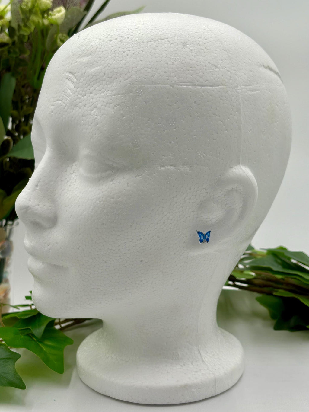 Blue Butterfly-shaped earrings on a mannequin head with green leaves in the background