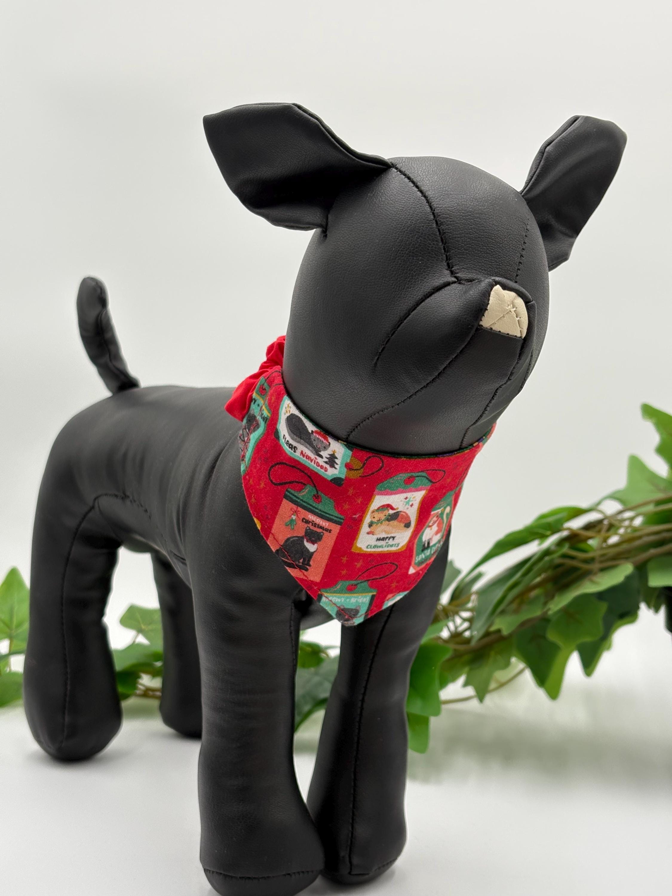 Black dog mannequin with a red bandana featuring cats on a white background standing next to a potted plant. 