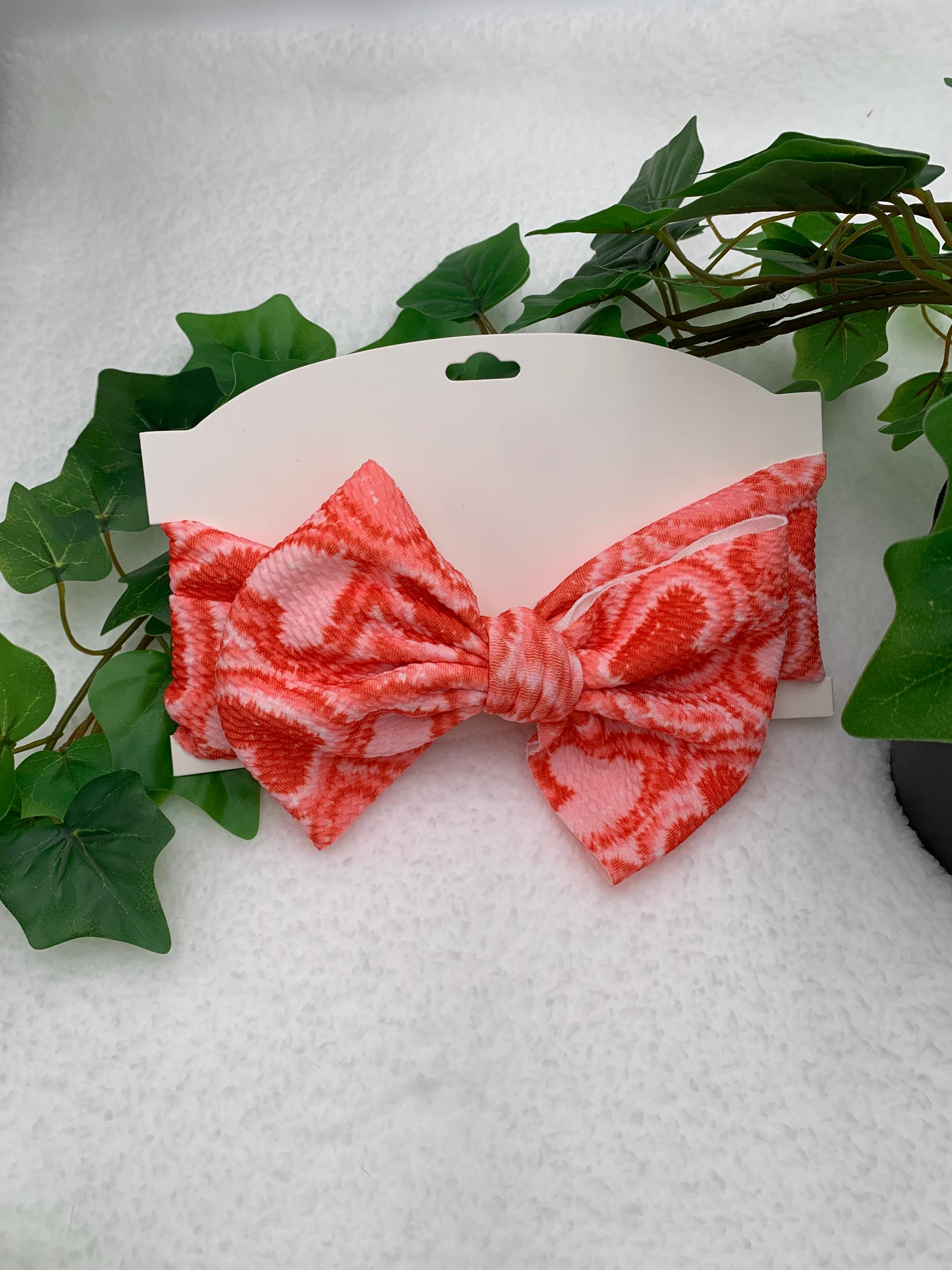 Red and Pink Headband with a decorative hearts themed big bow on a white cardstock against a white background