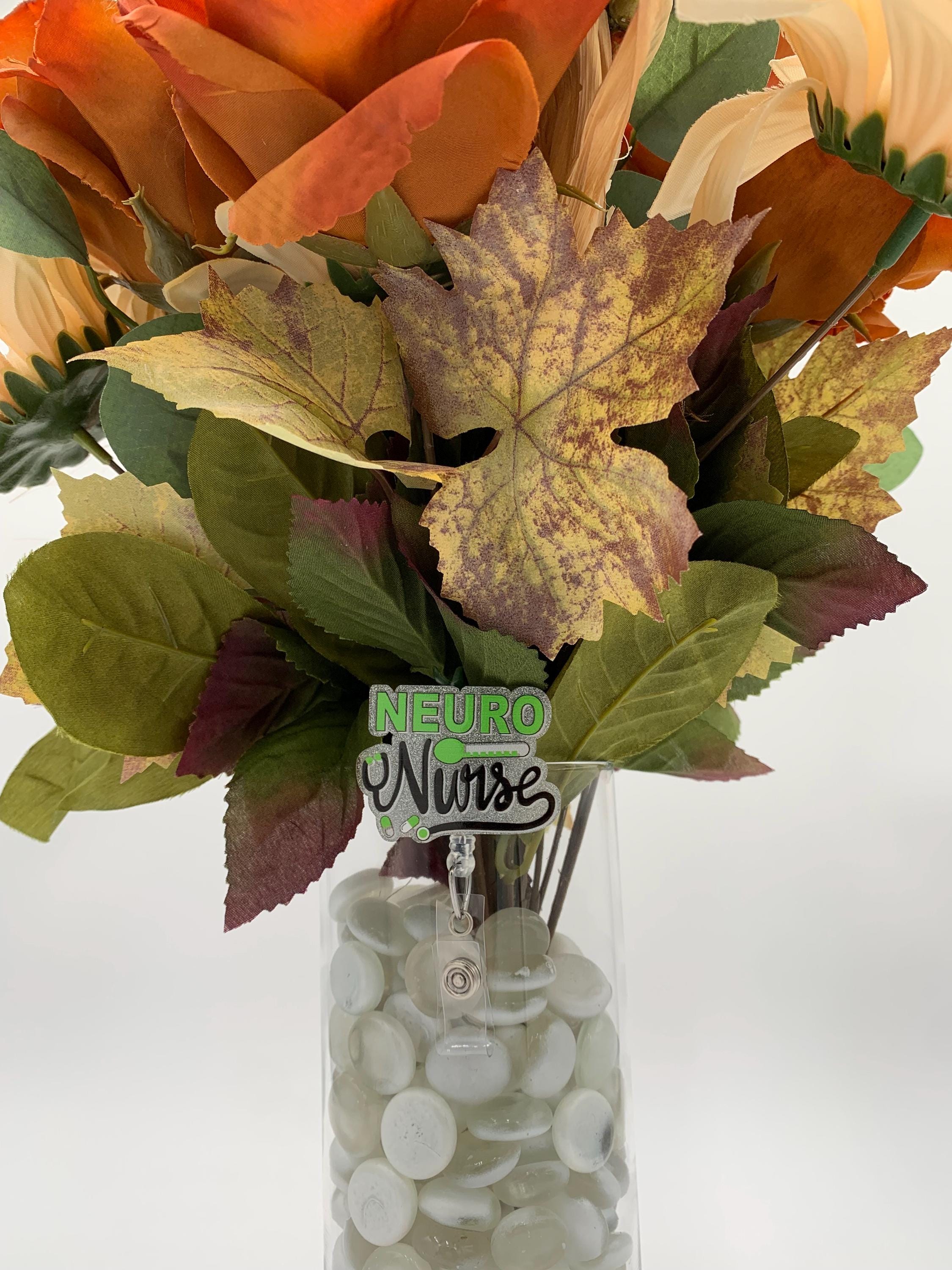 Bouquet of autumn-themed flowers with a 'Neuro Nurse' badge reel in a clear vase.