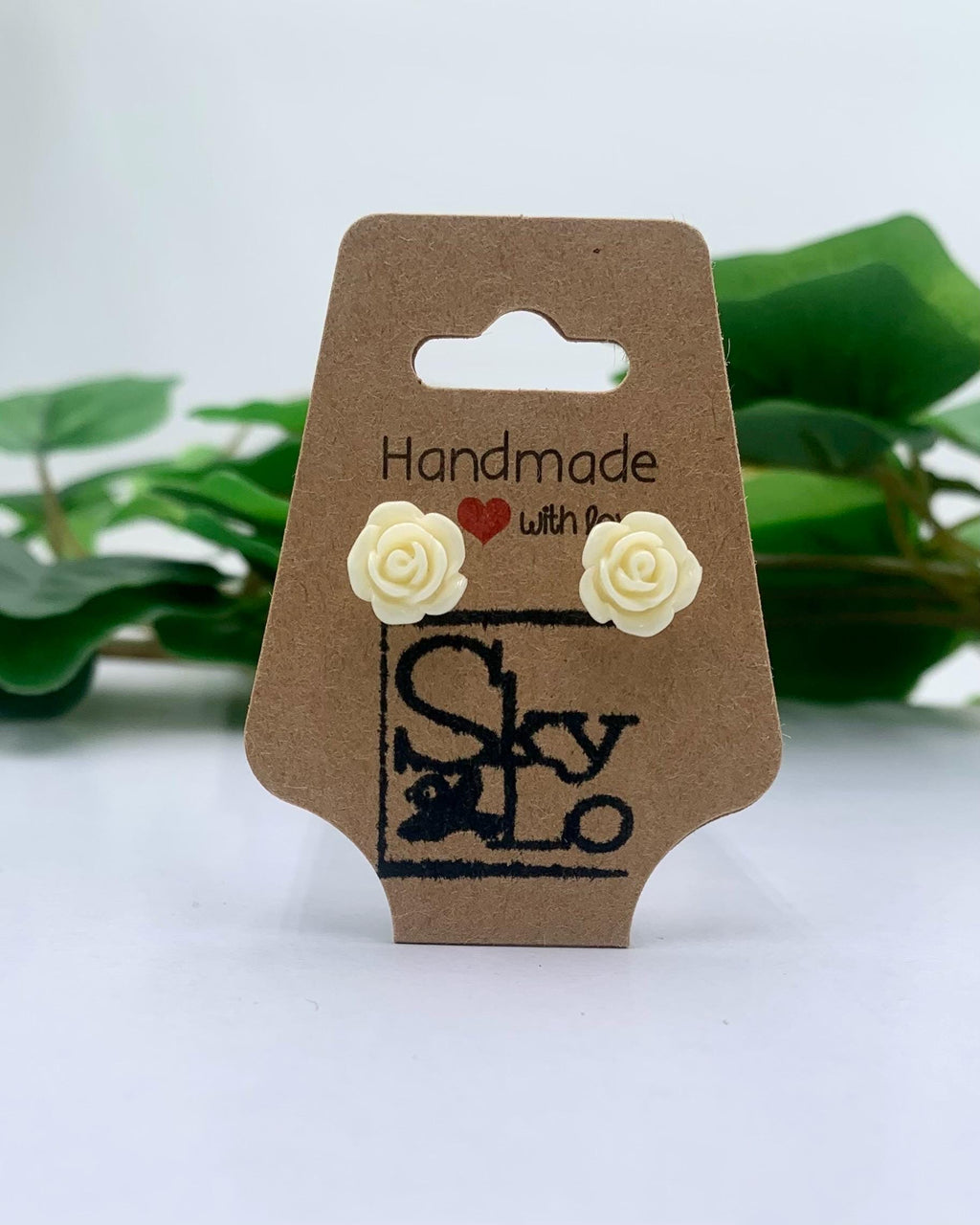 Pair of butter cream rose-shaped earrings on a 'Handmade with Love' branded card with green leaves in the background.