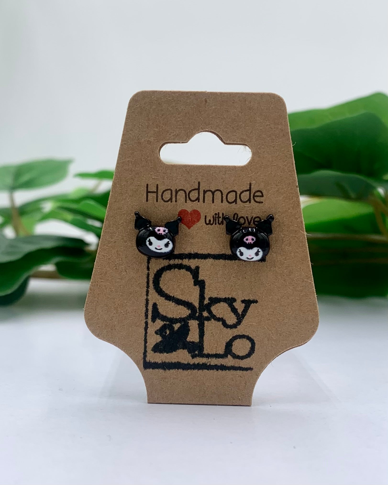 Pair of black and white cat-shaped earrings on a 'SkyLo' branded card with green leaves in the background.
