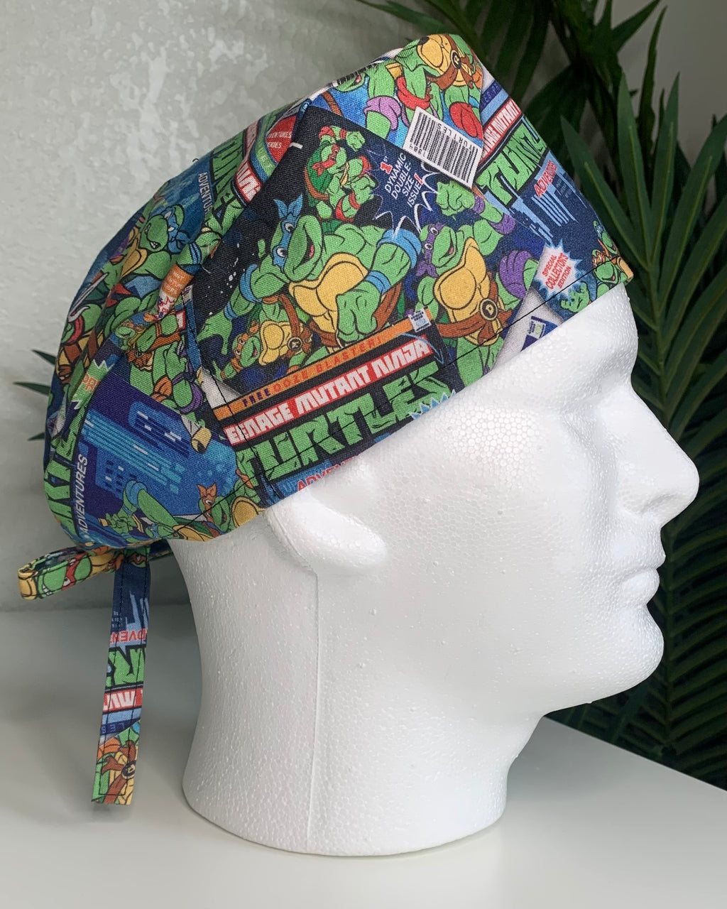 Colorful Teenage Mutant Ninja’ Turtles scrub cap on a mannequin head with a plant, against a white background
