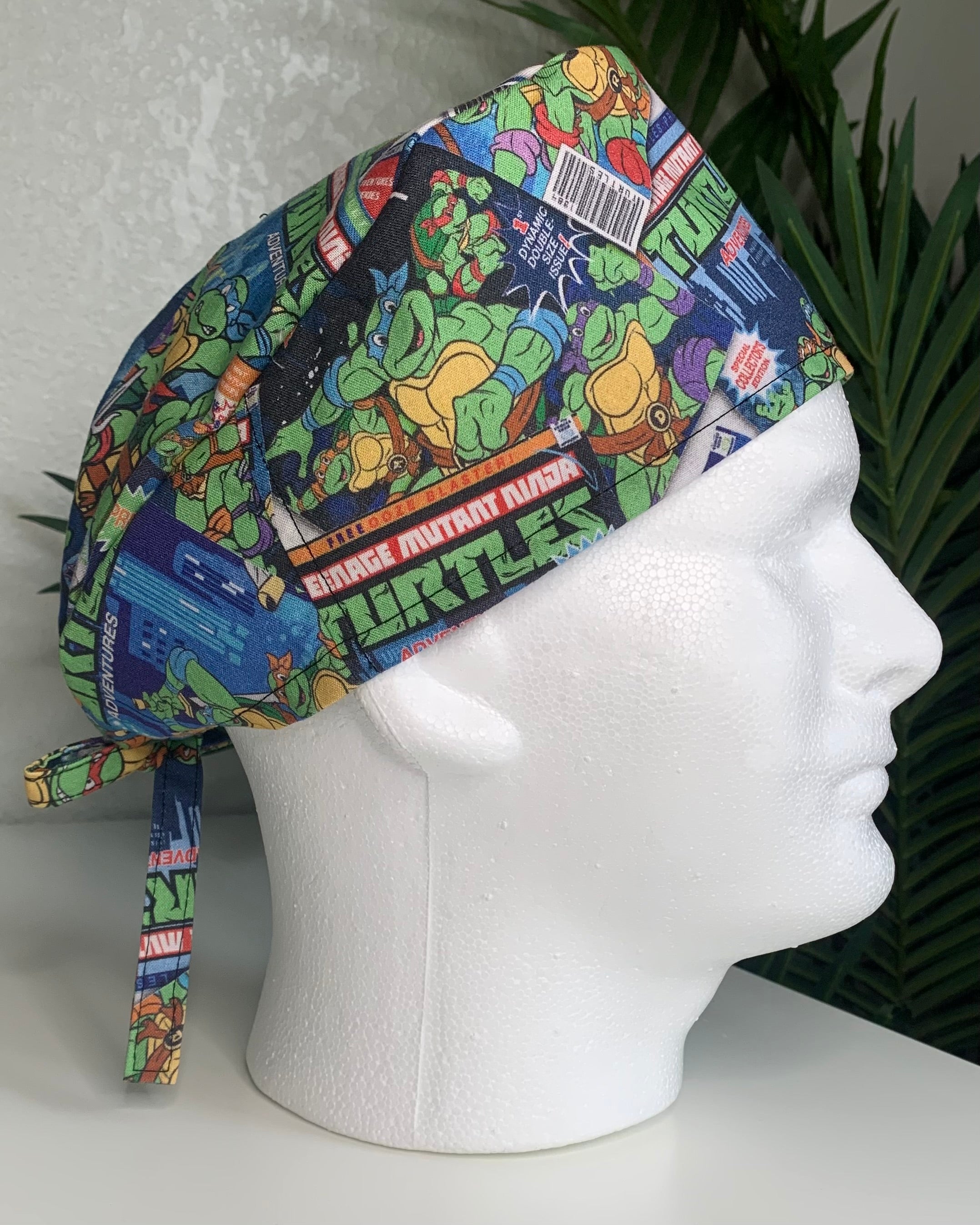 Colorful Teenage Mutant Ninja’ Turtles scrub cap on a mannequin head with a plant, against a white background