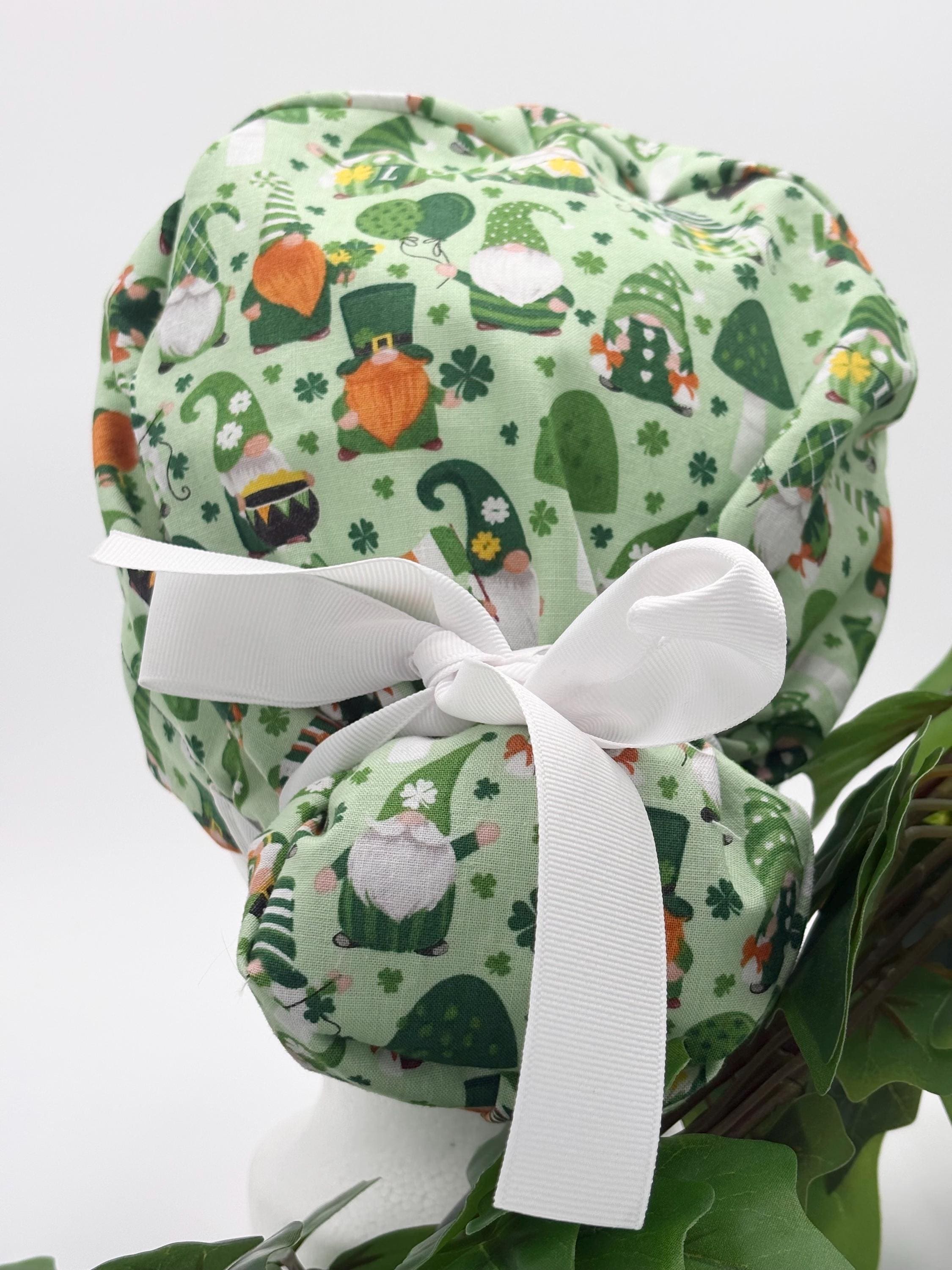 Green gnome scrub cap with white ribbon on a mannequin head against a white background with plant