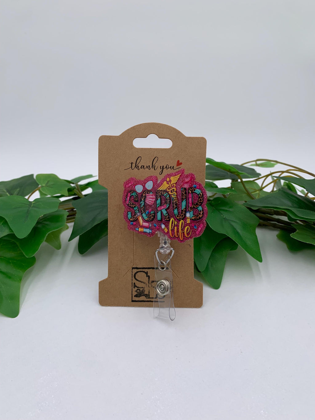 Badge reel with 'Scrub life' text on a cardboard backing with green leaves in the background