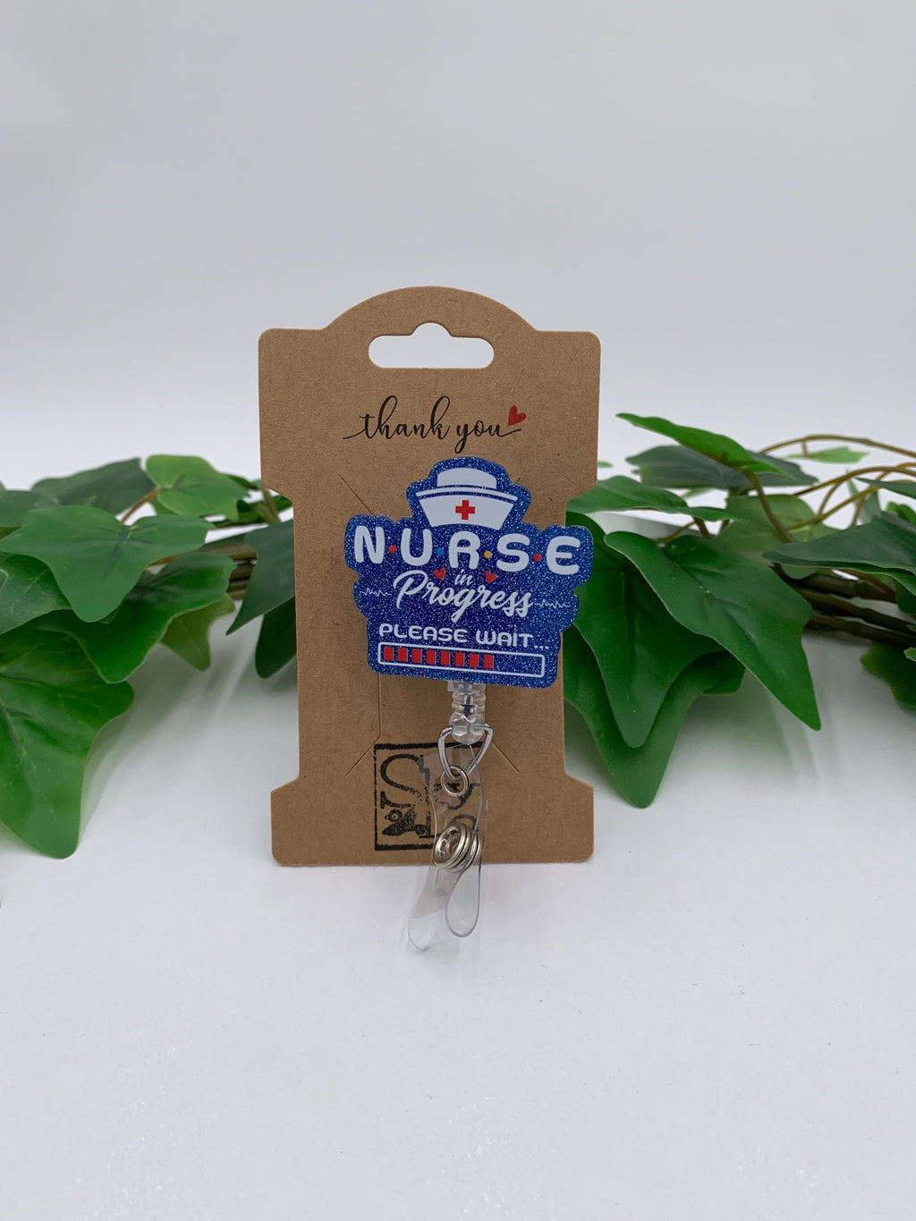Nurse-themed badge reel on a cardboard holder with green leaves in the background