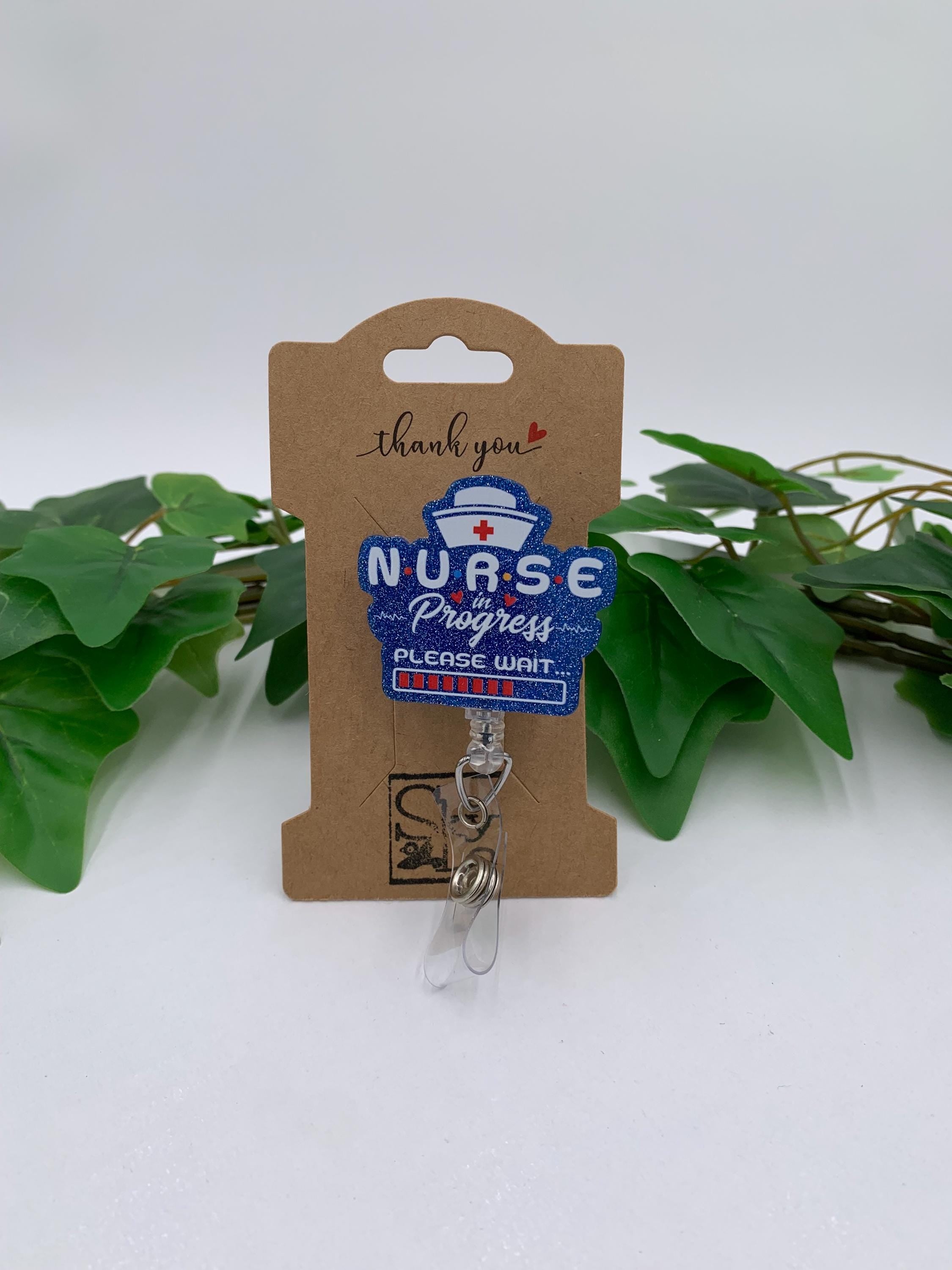 Nurse-themed badge reel on a cardboard holder with green leaves in the background