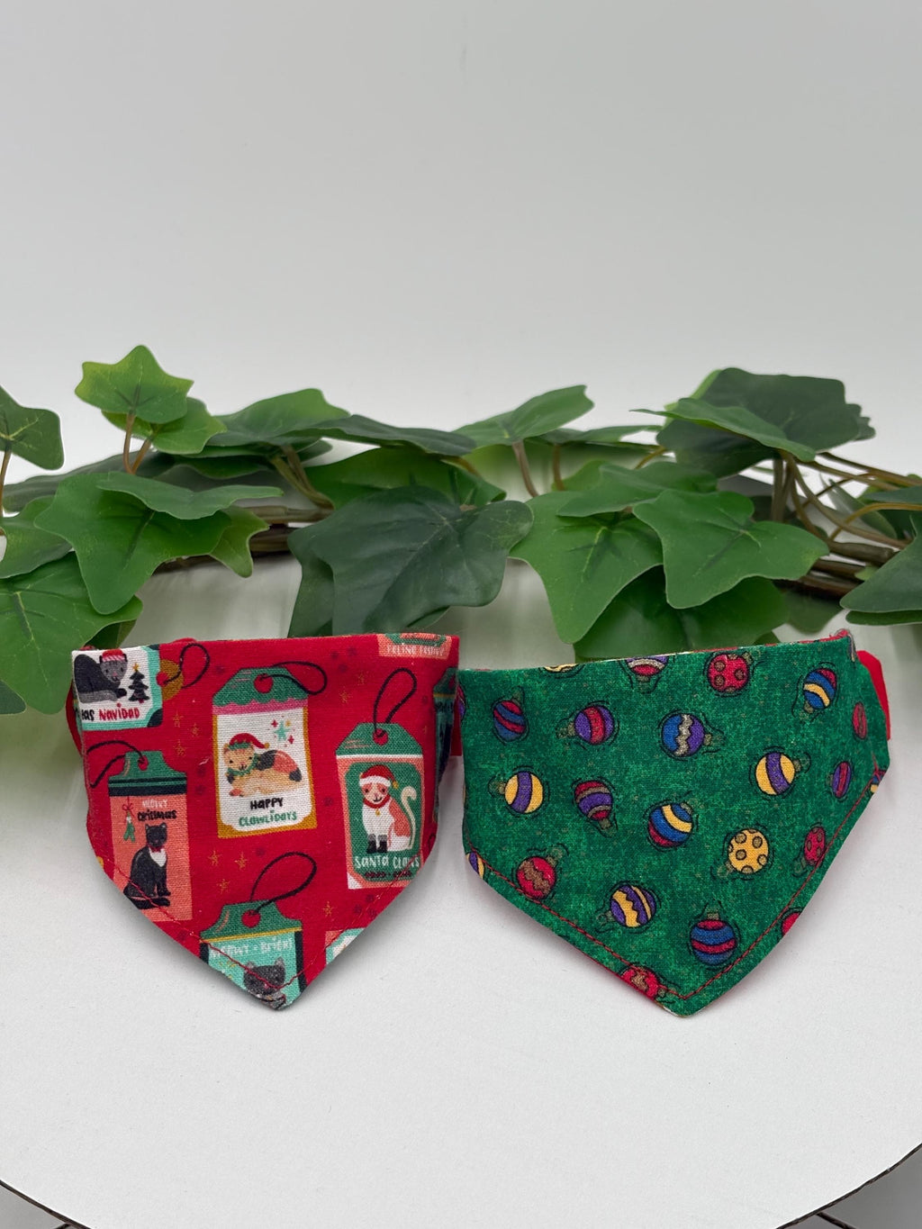 Two colorful scrunchie pet bandanas on a white surface with green leaves in the background