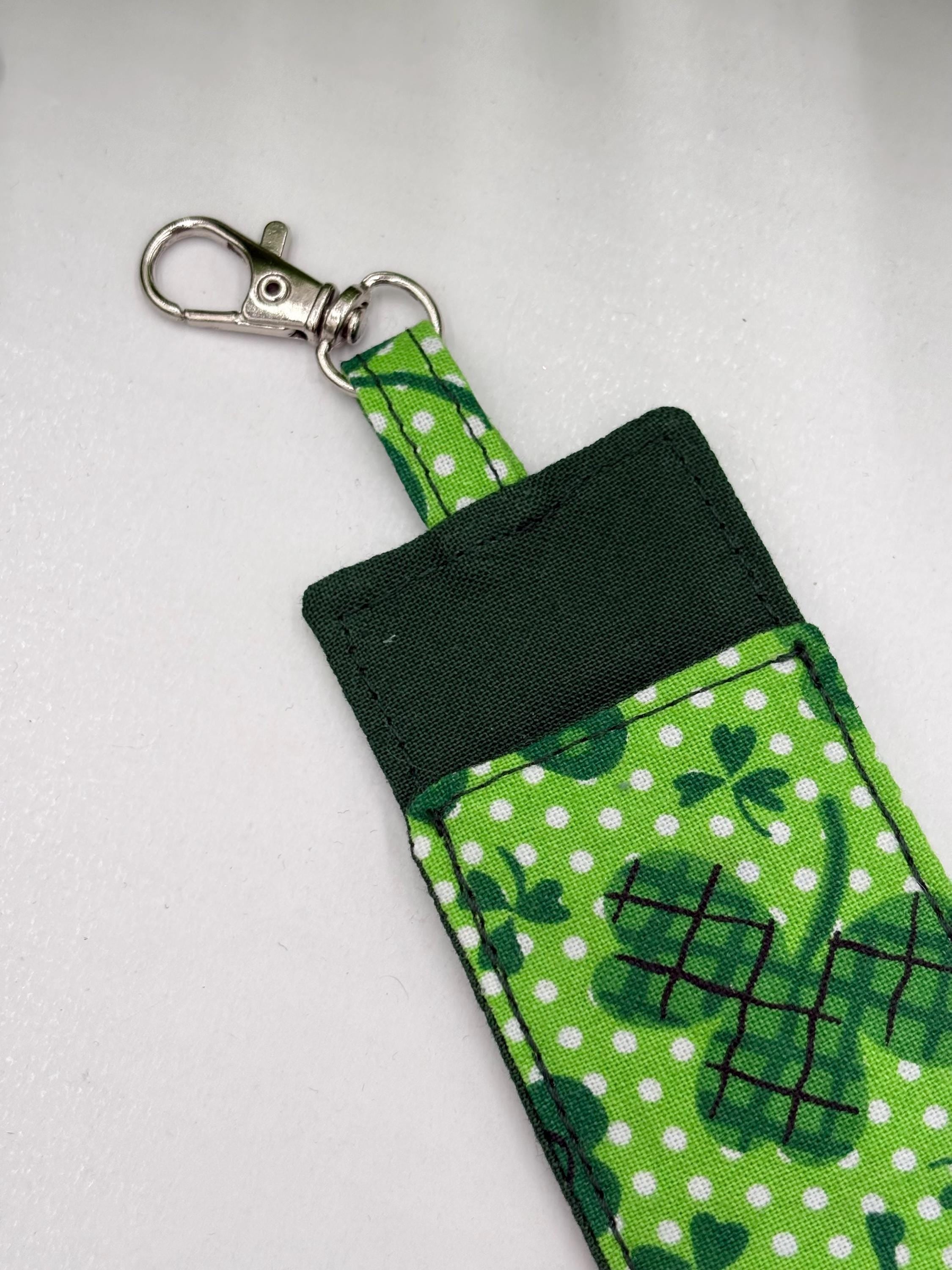 close up of lobster clasps of Green shamrock-patterned chapstick holder on a white surface with green leaves in the background
