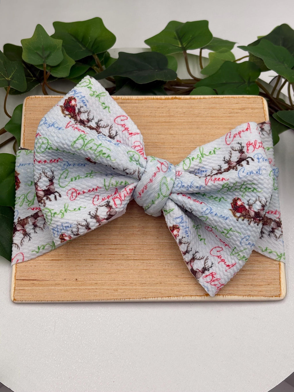 Headband with a decorative christmas themed big bow headband on a wooden plank against a white background