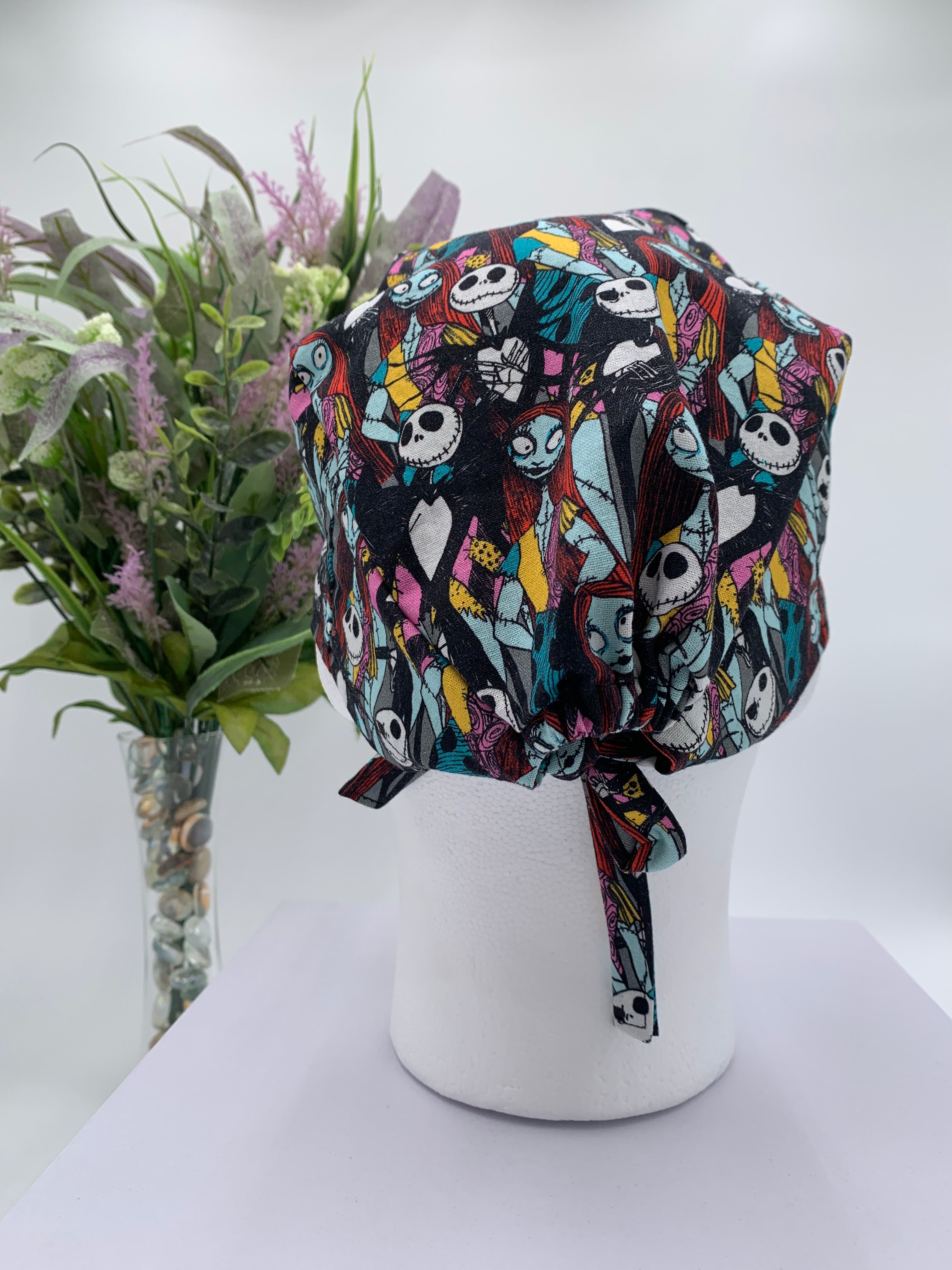 Mannequin head wearing a nightmare before christmas scrub cap with a decorative plant in the background.