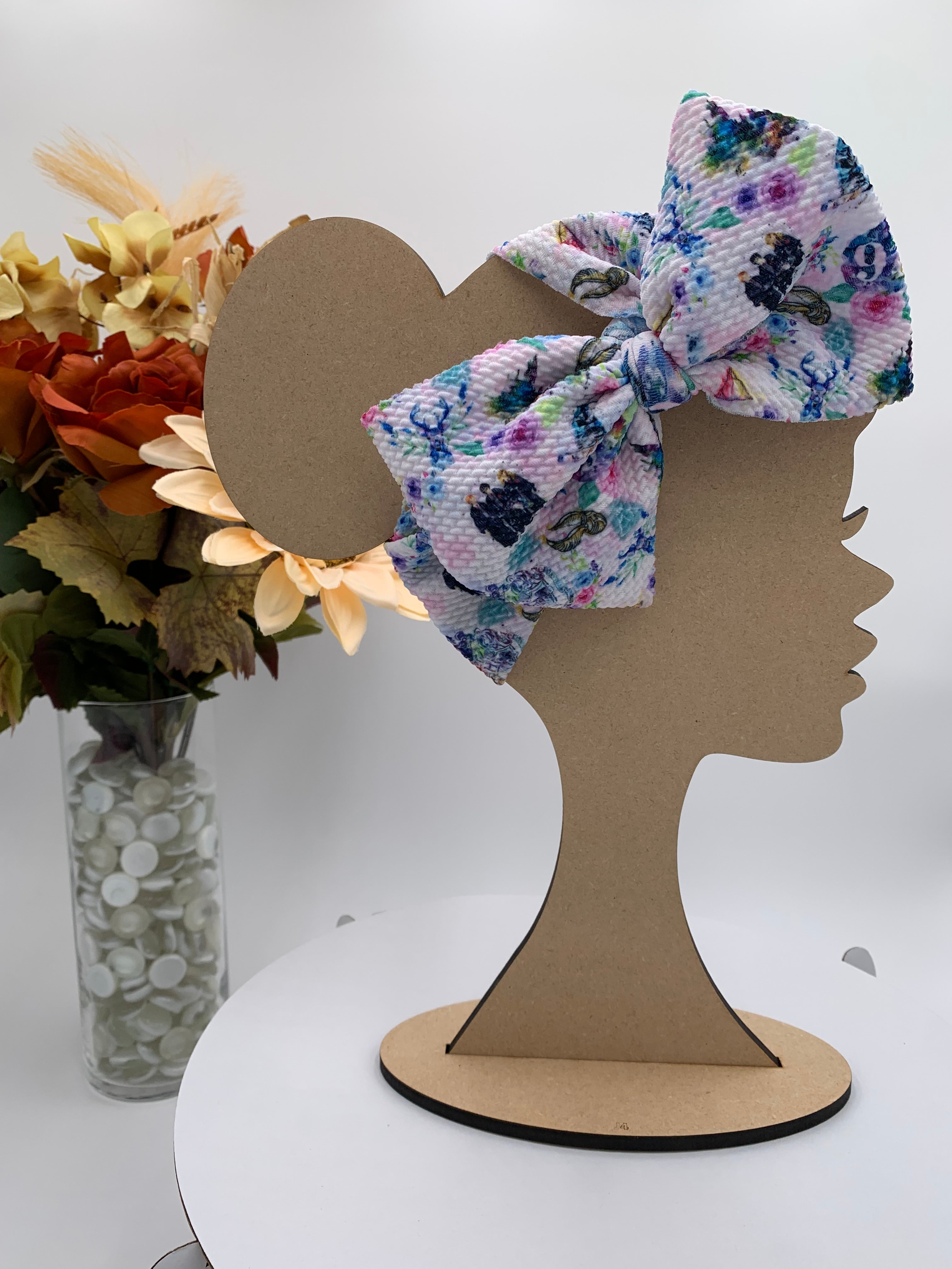 Fantasy wizard themed big bow headband on a mannequin head with a white background and greenery 