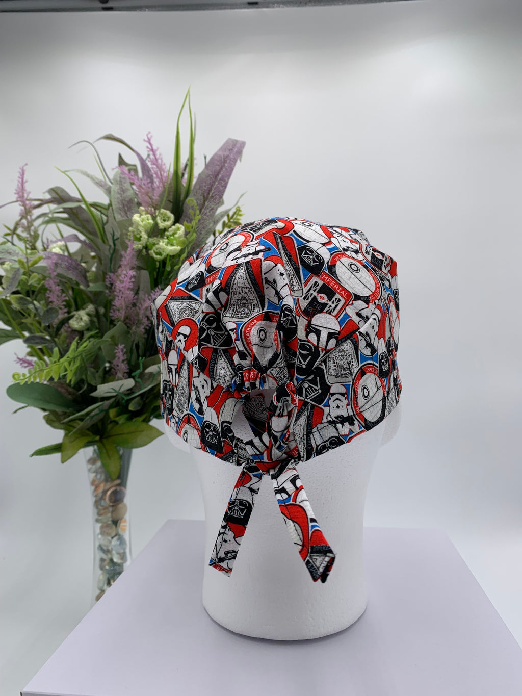 Colorful Star Wars scrub cap on a mannequin head with flowers, against a white background