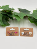 Two sets of metallic Heart-shaped earrings on display with a brand label against a white background with green leaves.