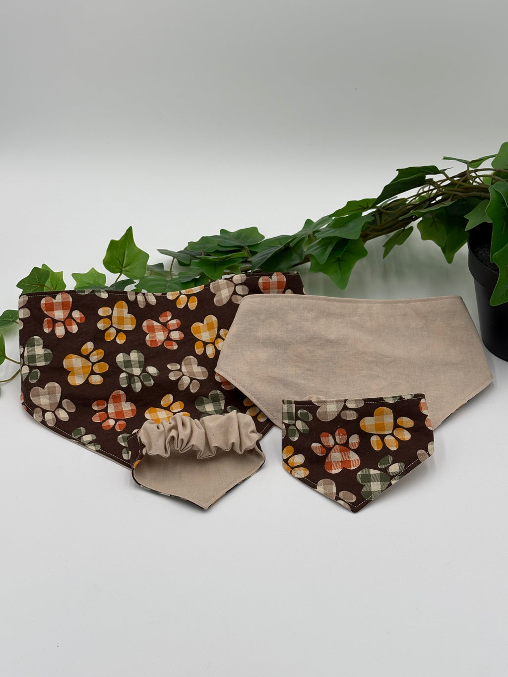 Dog bandanas with paw print and plaid pattern on a white background with a green potted plant