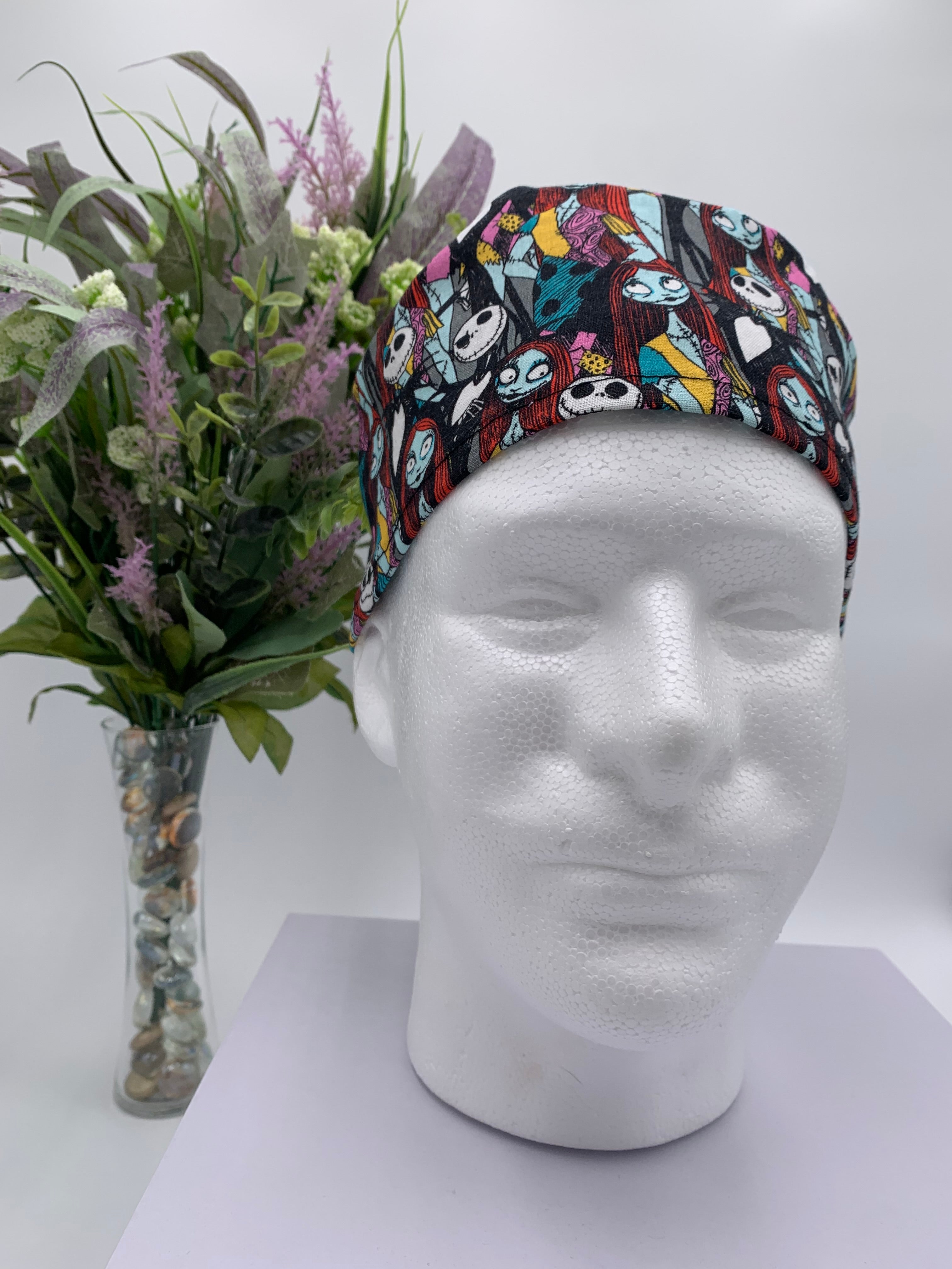 Mannequin head wearing a nightmare before christmas scrub cap with a decorative plant in the background.