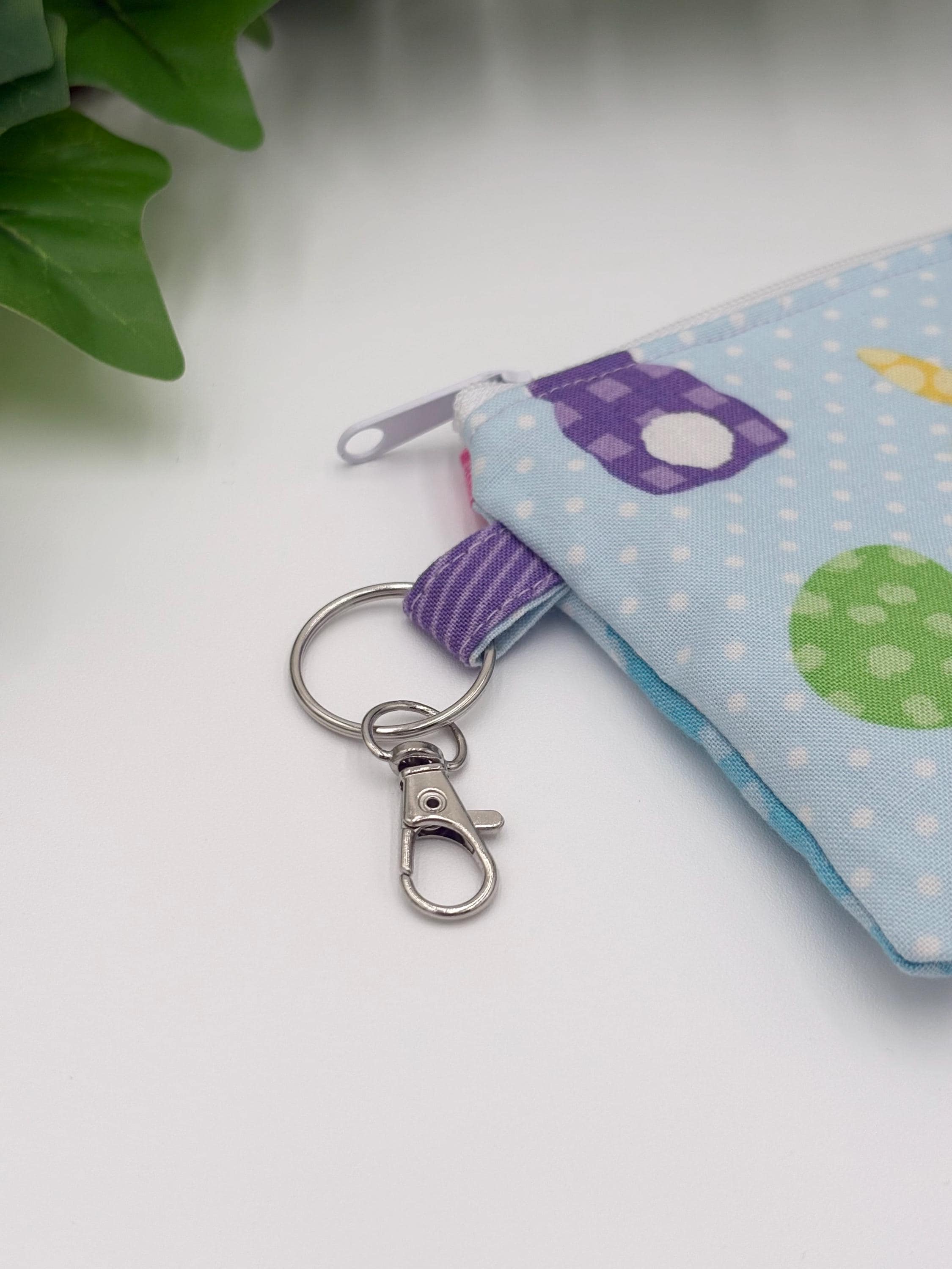close up of keychain on Small coin purse keychain with blue and pastel eggs and bunnies pattern on a white background with green leaves