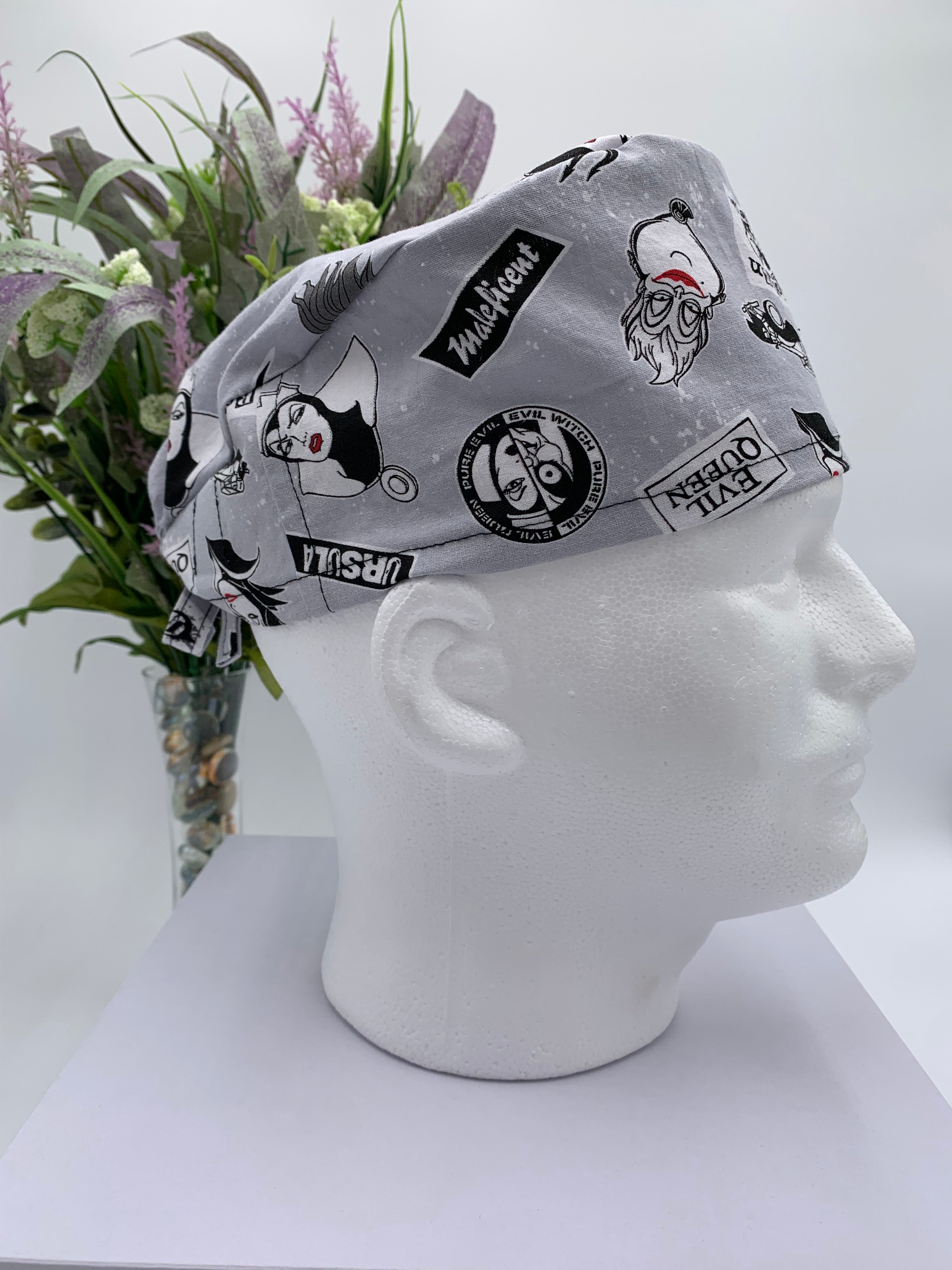 Gray scrub cap with black graphics on a mannequin head against a white background with flowers in the background