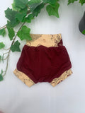 Maroon baby bloomers with beige patterned waistband on a white background with greenery