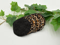 Set of five reusable makeup remover pads with leopard print and black fabric, surrounded by green leaves on a white background.