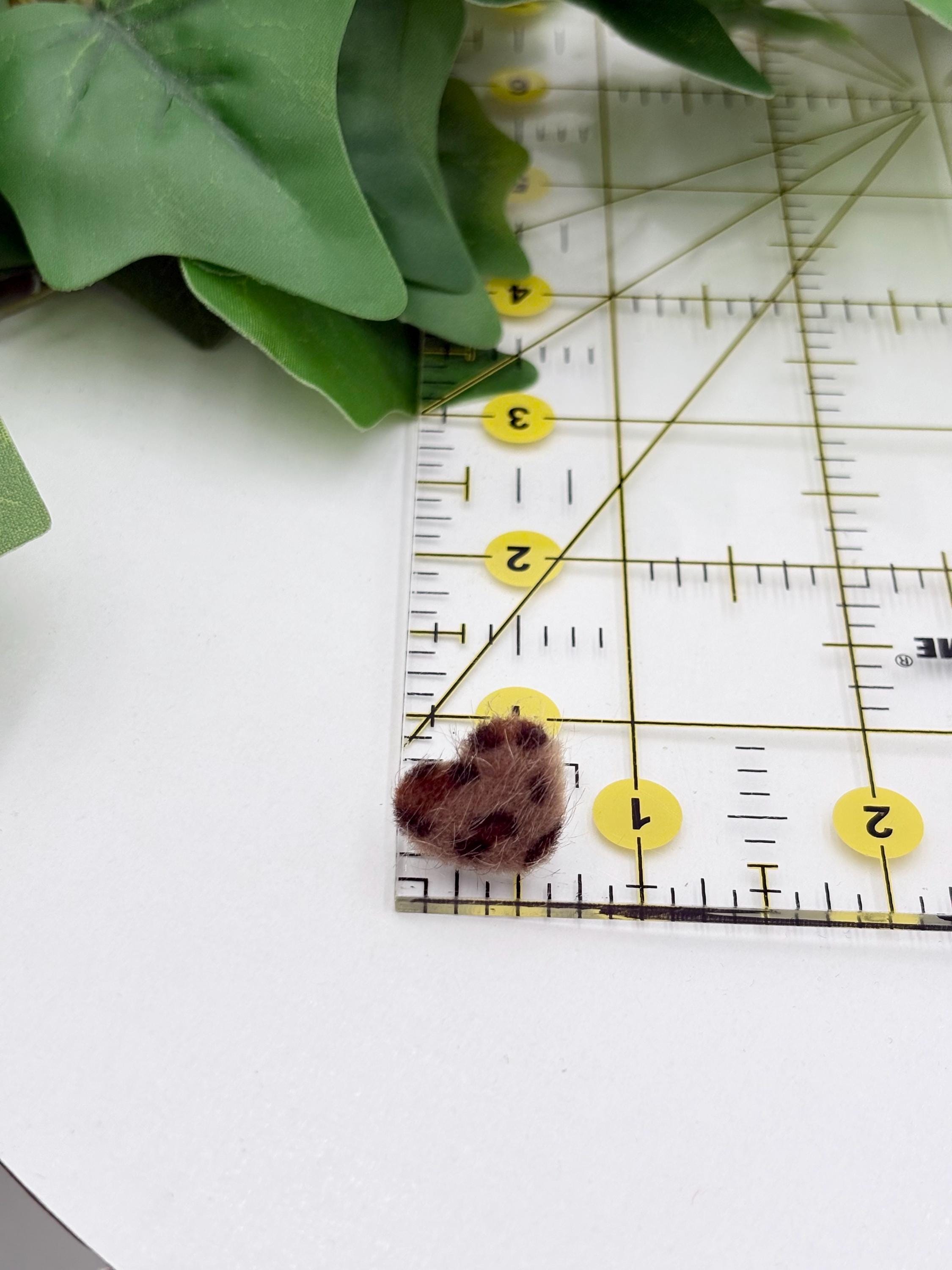 Dark brown faux fur leopard print earring on a ruler with green leaves in the background
