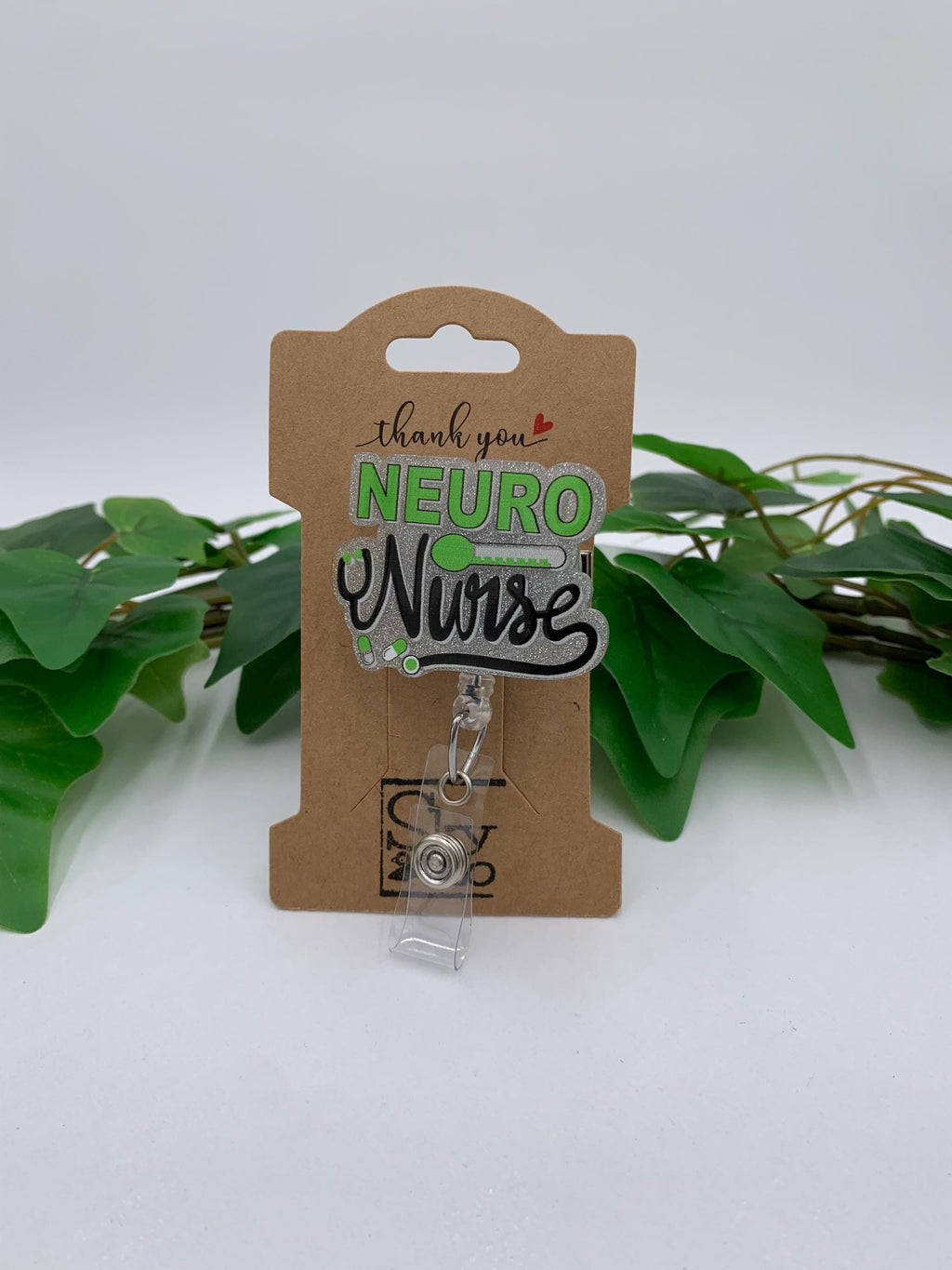 Neuro Nurse badge holder on a cardboard backing with green leaves in the background