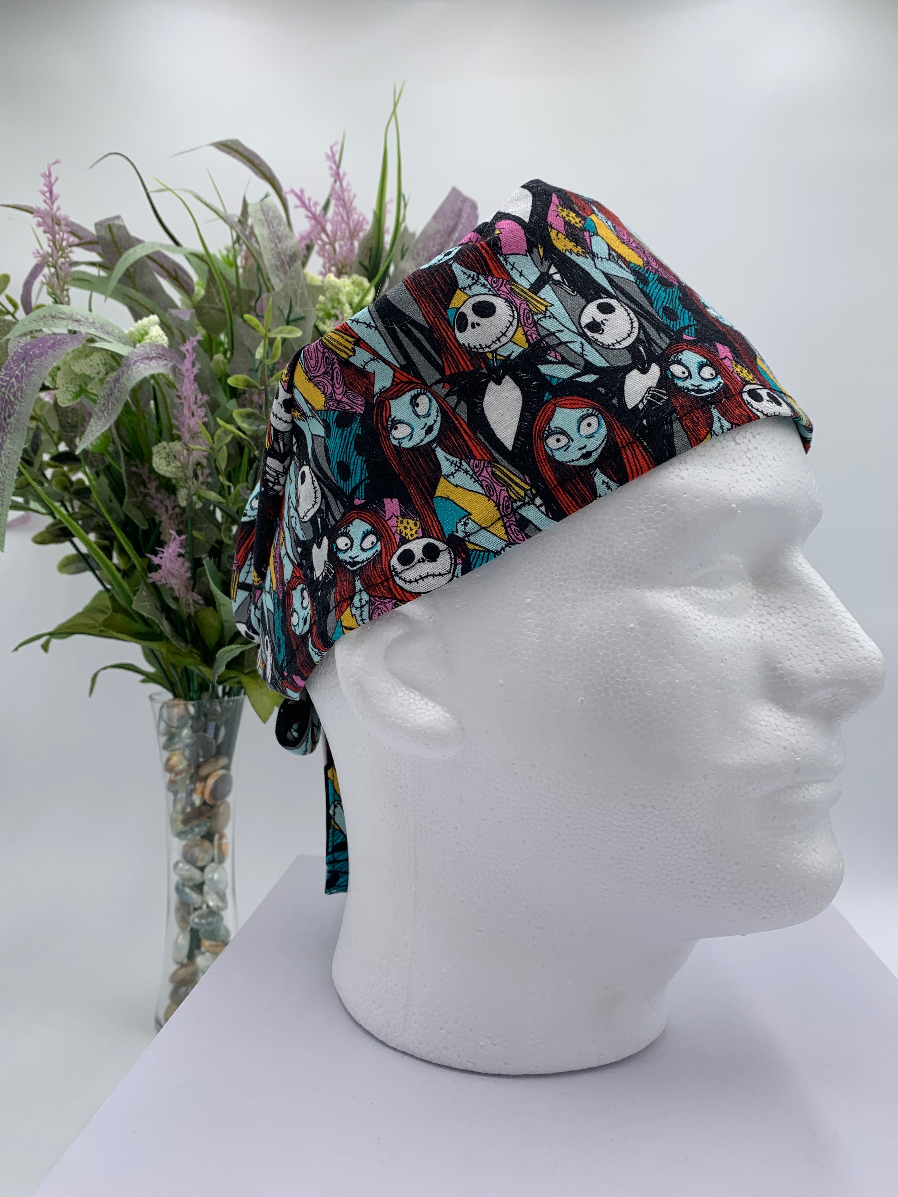 Mannequin head wearing a nightmare before christmas scrub cap with a decorative plant in the background.