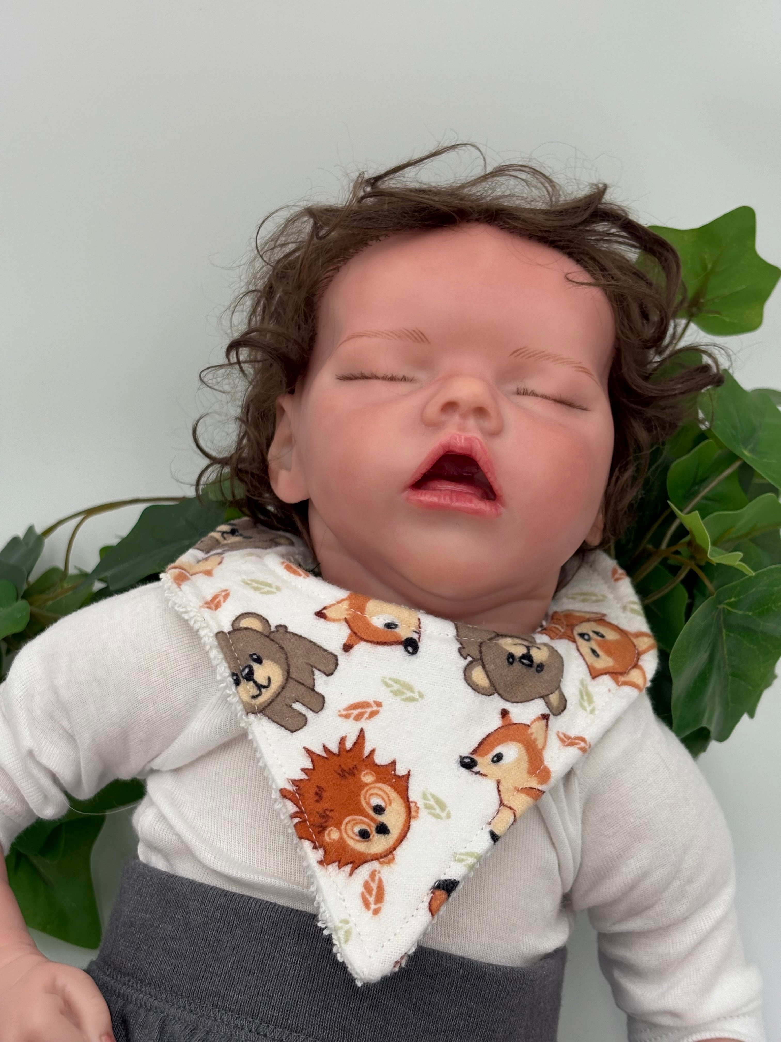 Baby doll wearing a bib with animal patterns against a white background and green leaves
