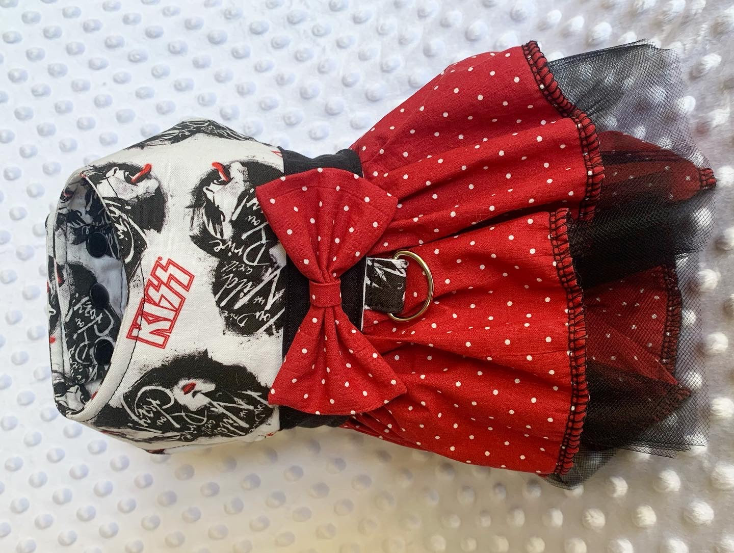 A red polka dot ruffle harness dress with heavy metal band design on it on a white textured background