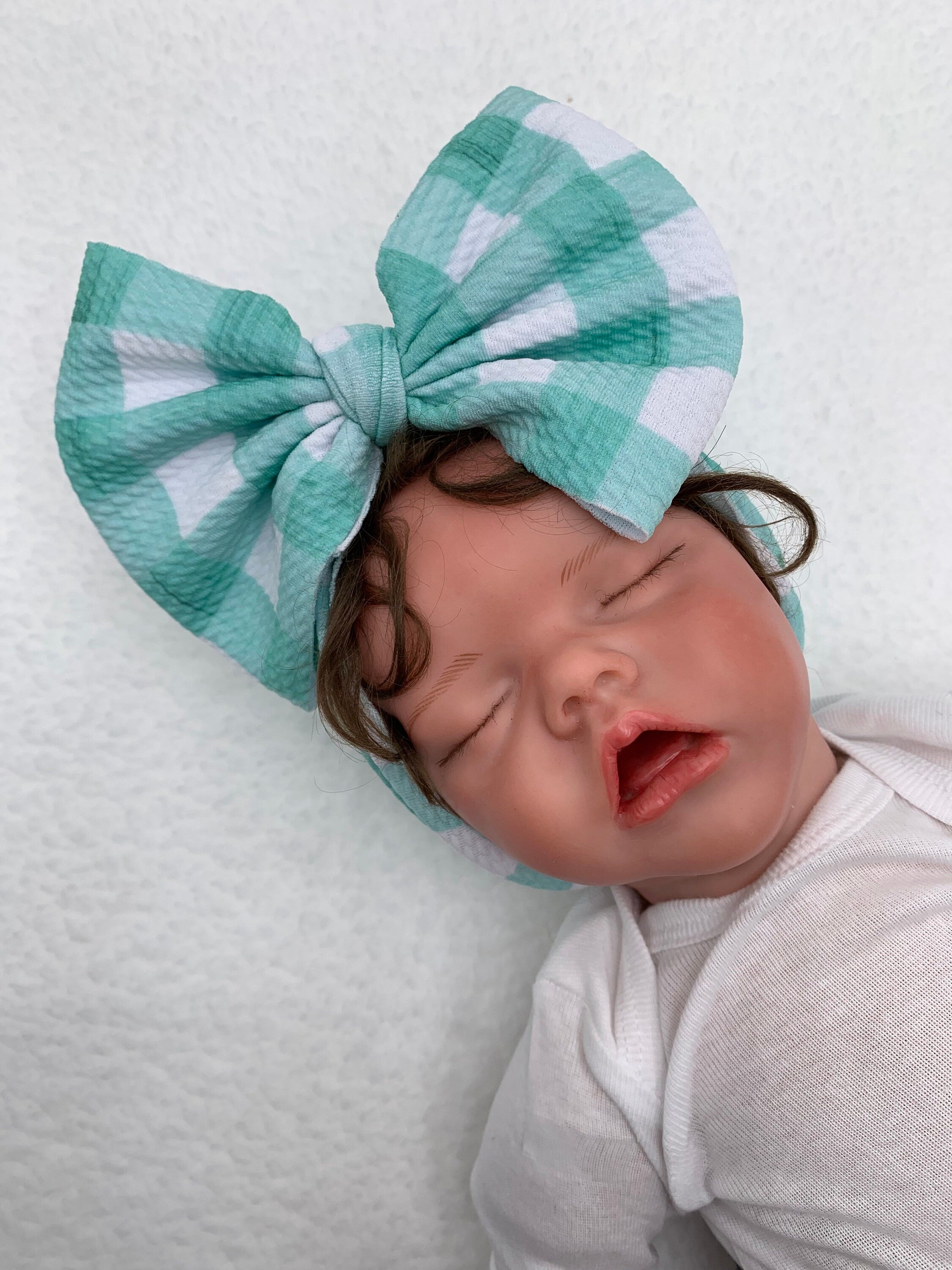 close up of Newborn baby wearing a large blue and white checkered bow headband on a white background