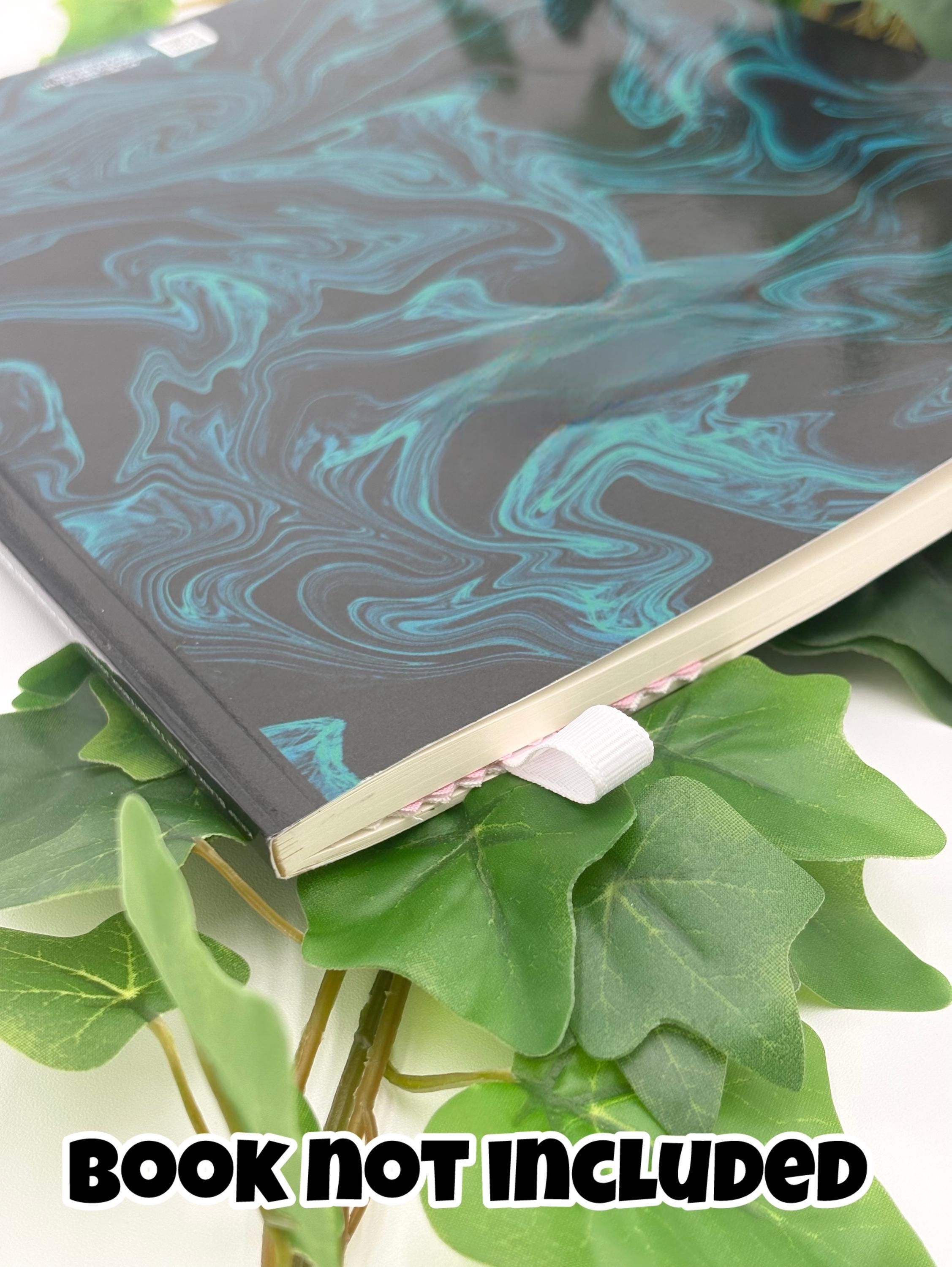 Marbled notebook on green leaves with 'Book Not Included' text showing bookmark ribbon inside book