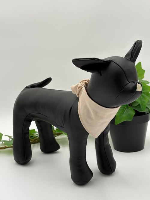 Black dog mannequin wearing a khaki scrunchie bandana on a white background with green leaves.