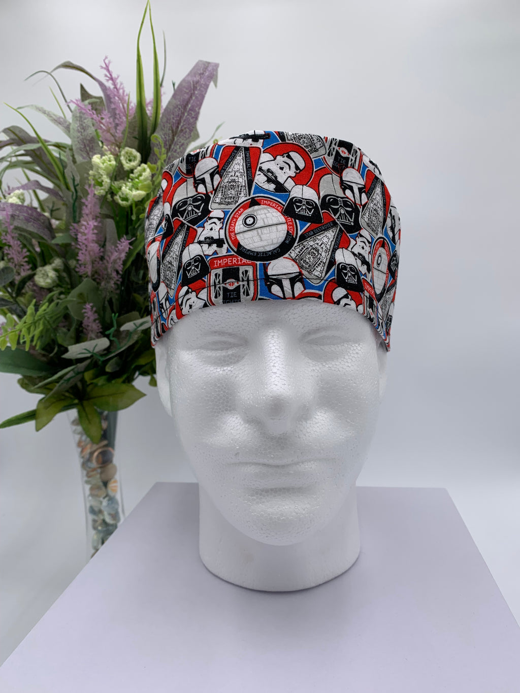 Colorful Star Wars scrub cap on a mannequin head with flowers, against a white background