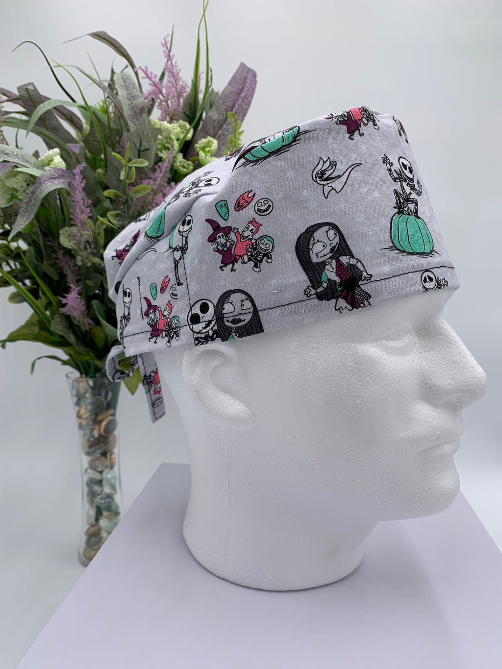 Mannequin head wearing a nightmare before christmas scrub cap with a decorative plant in the background.