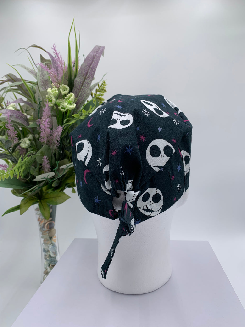Mannequin head wearing a jack skellington scrub cap with a decorative plant in the background.