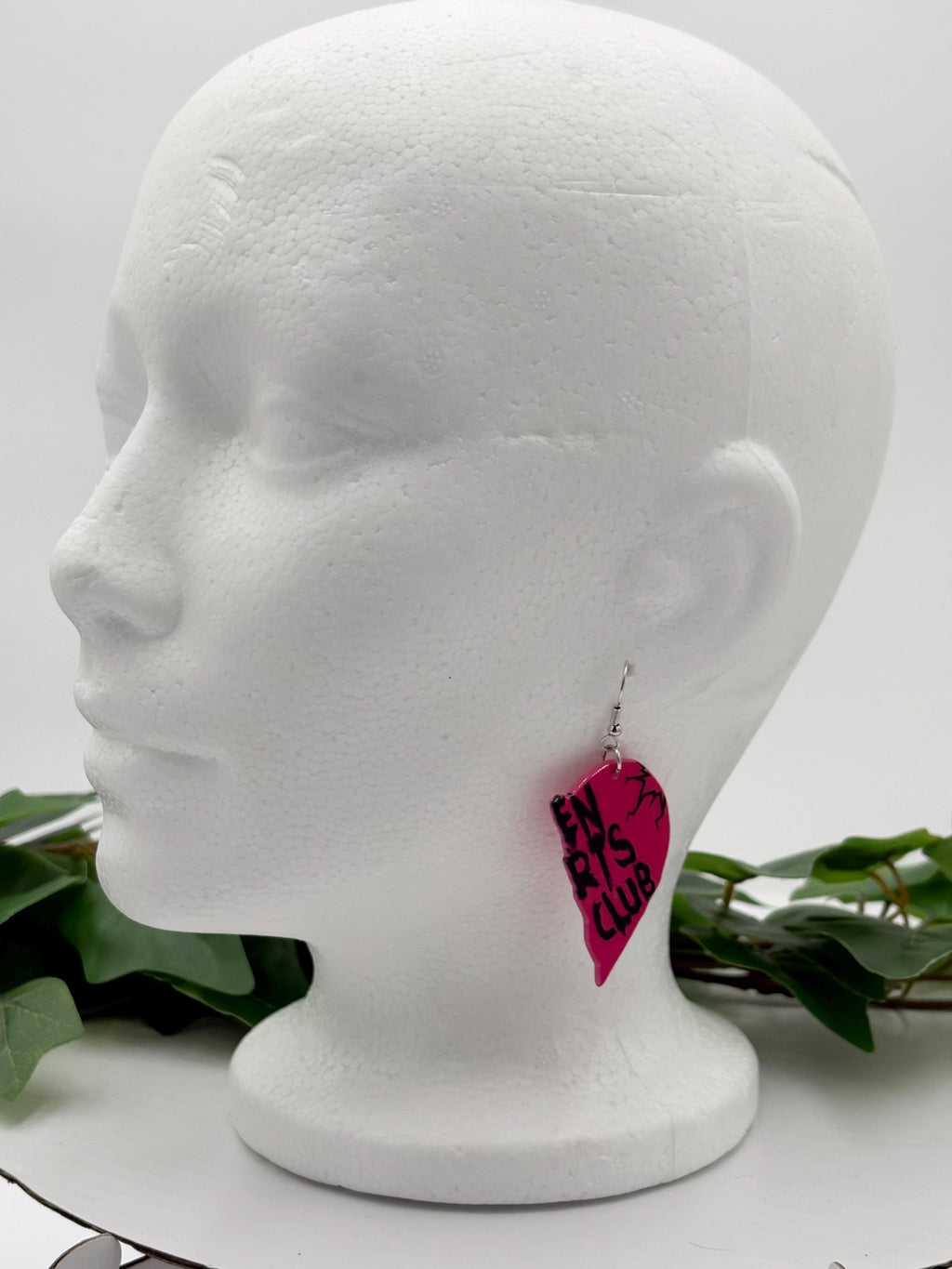 Mannequin head wearing pink heart-shaped earrings with text on a white background