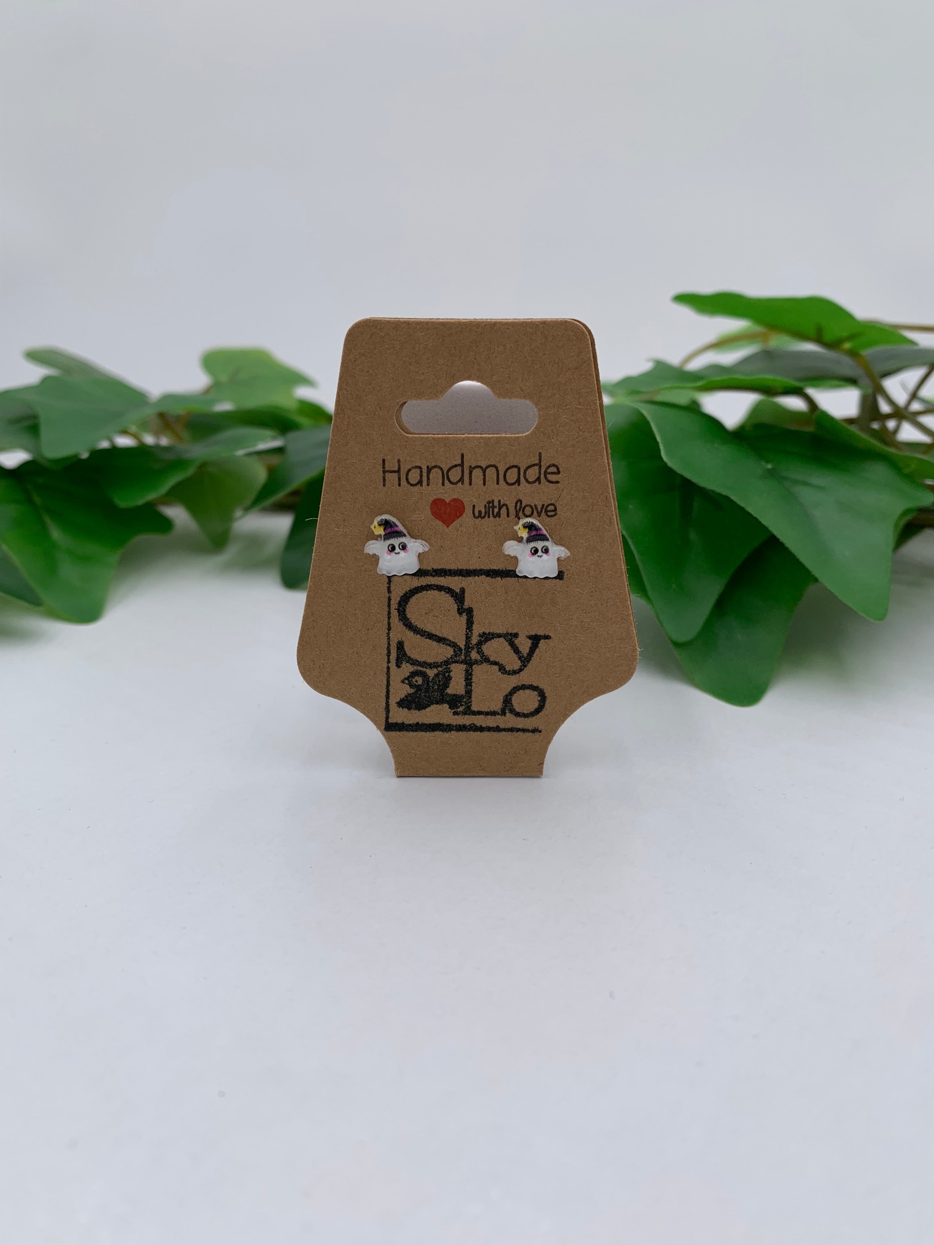 Pair of Ghost Witch earrings on a 'Handmade with Love' branded card with green leaves in the background