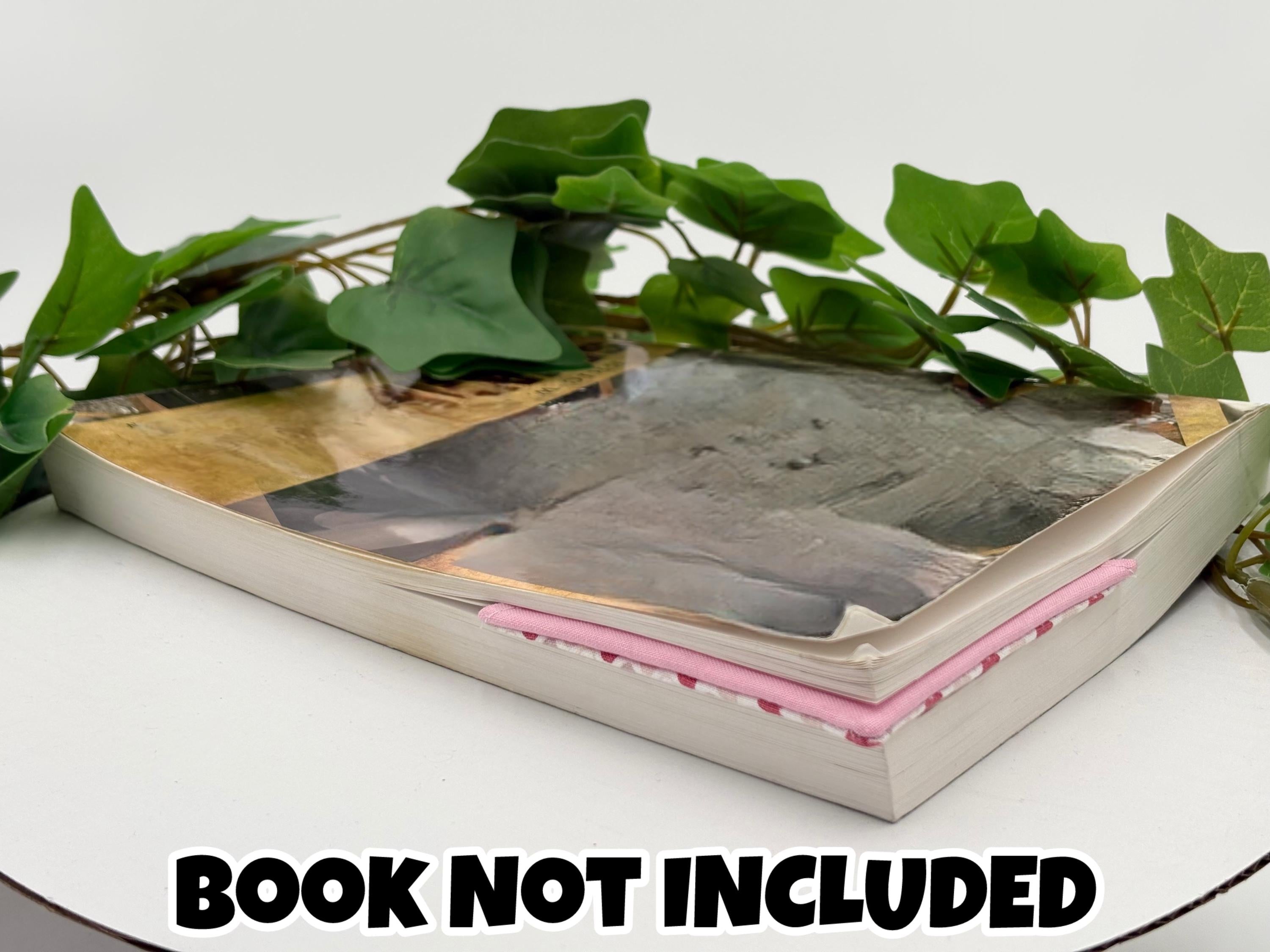Book with pink corner bookmark attached with green leaves on a white surface, text 'Book Not Included' at the bottom.