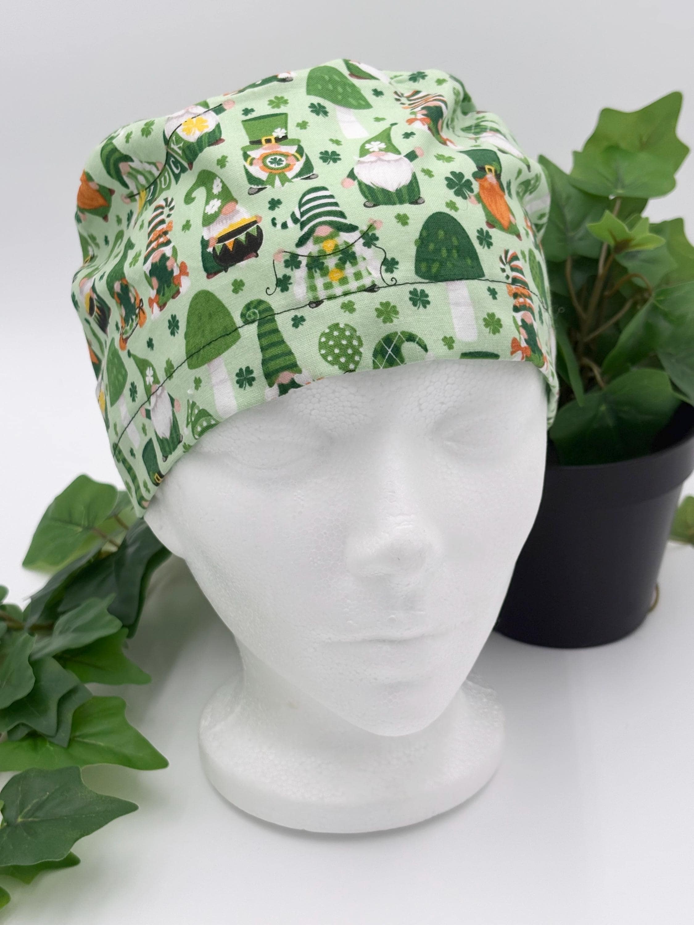 Green gnome scrub cap on a mannequin head against a white background with plant
