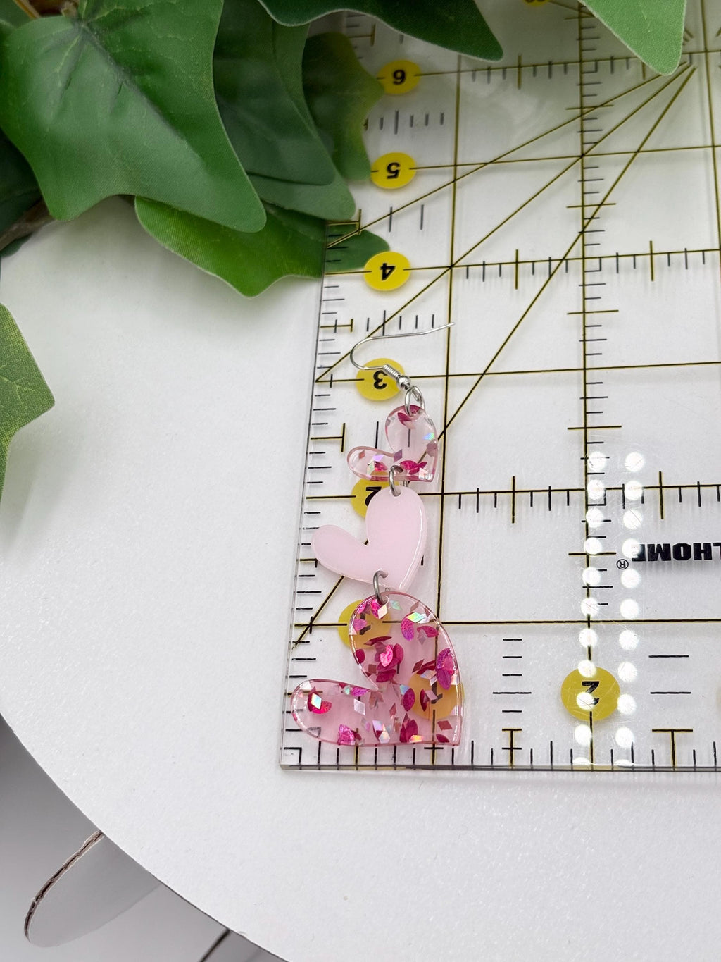 Pink heart shaped dangle earrings on a white surface with a ruler for scale.