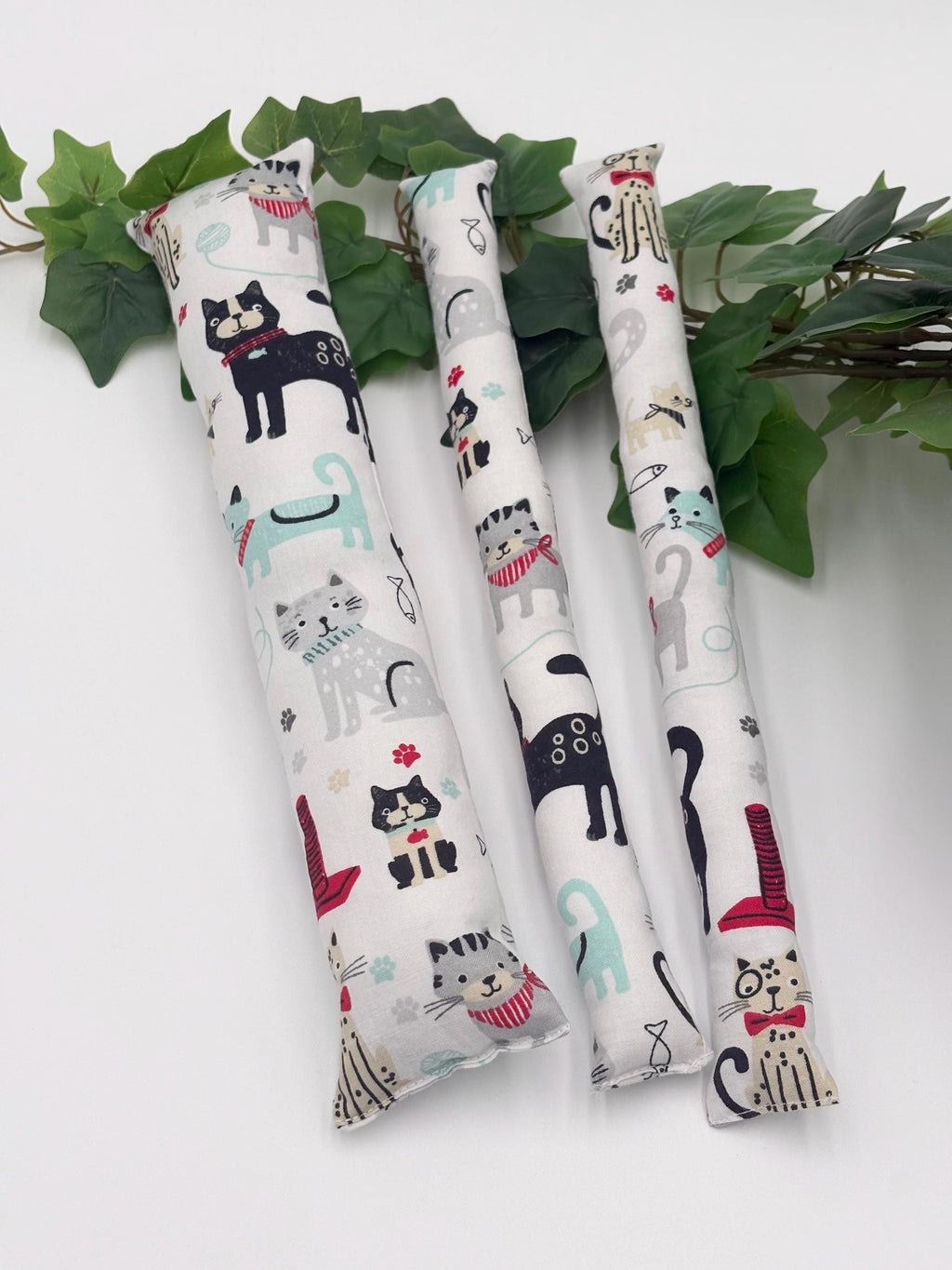Three cylindrical catnip toys with cat illustrations on a white background with green leaves.
