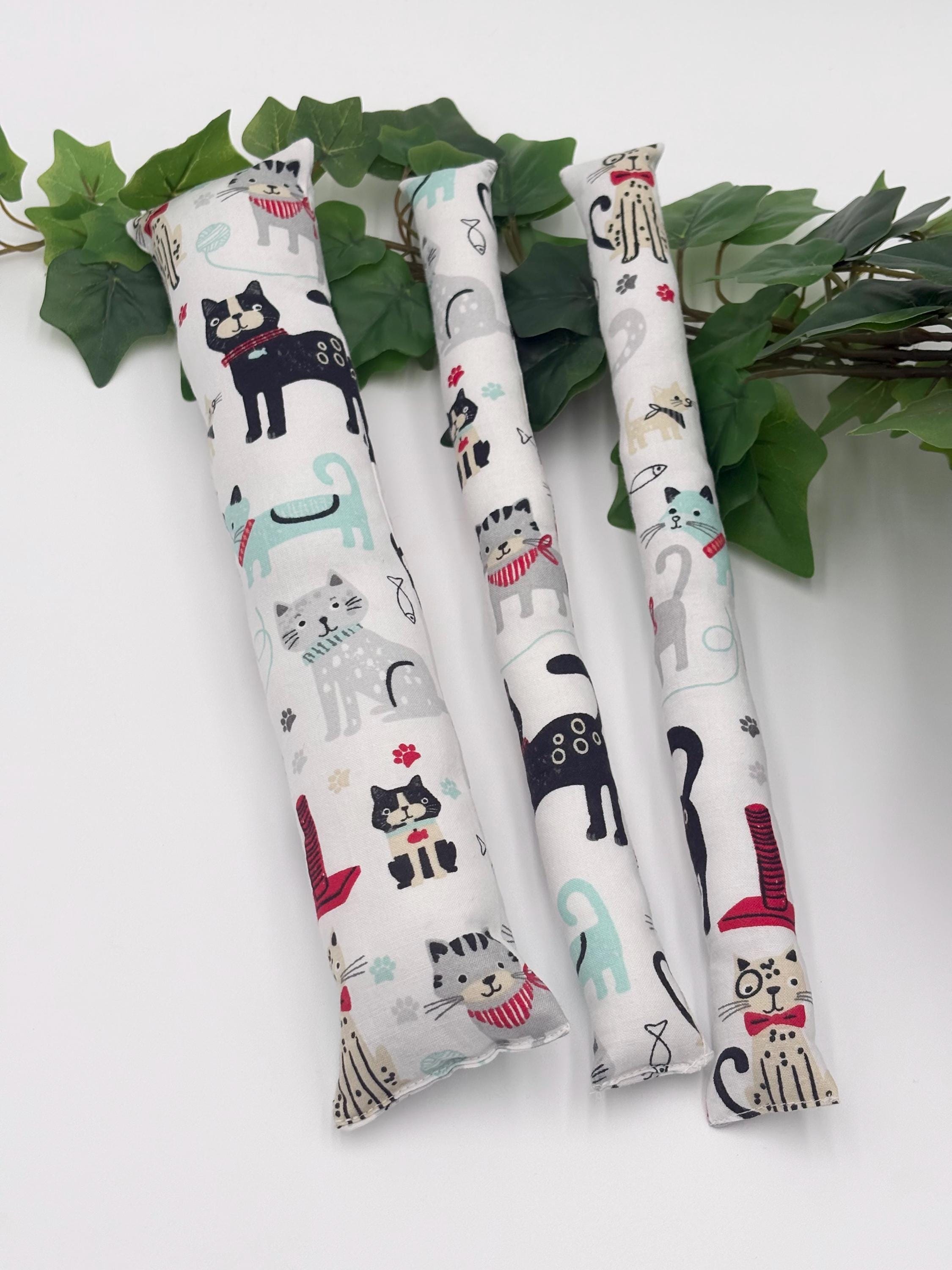 Three cylindrical catnip toys with cat illustrations on a white background with green leaves.