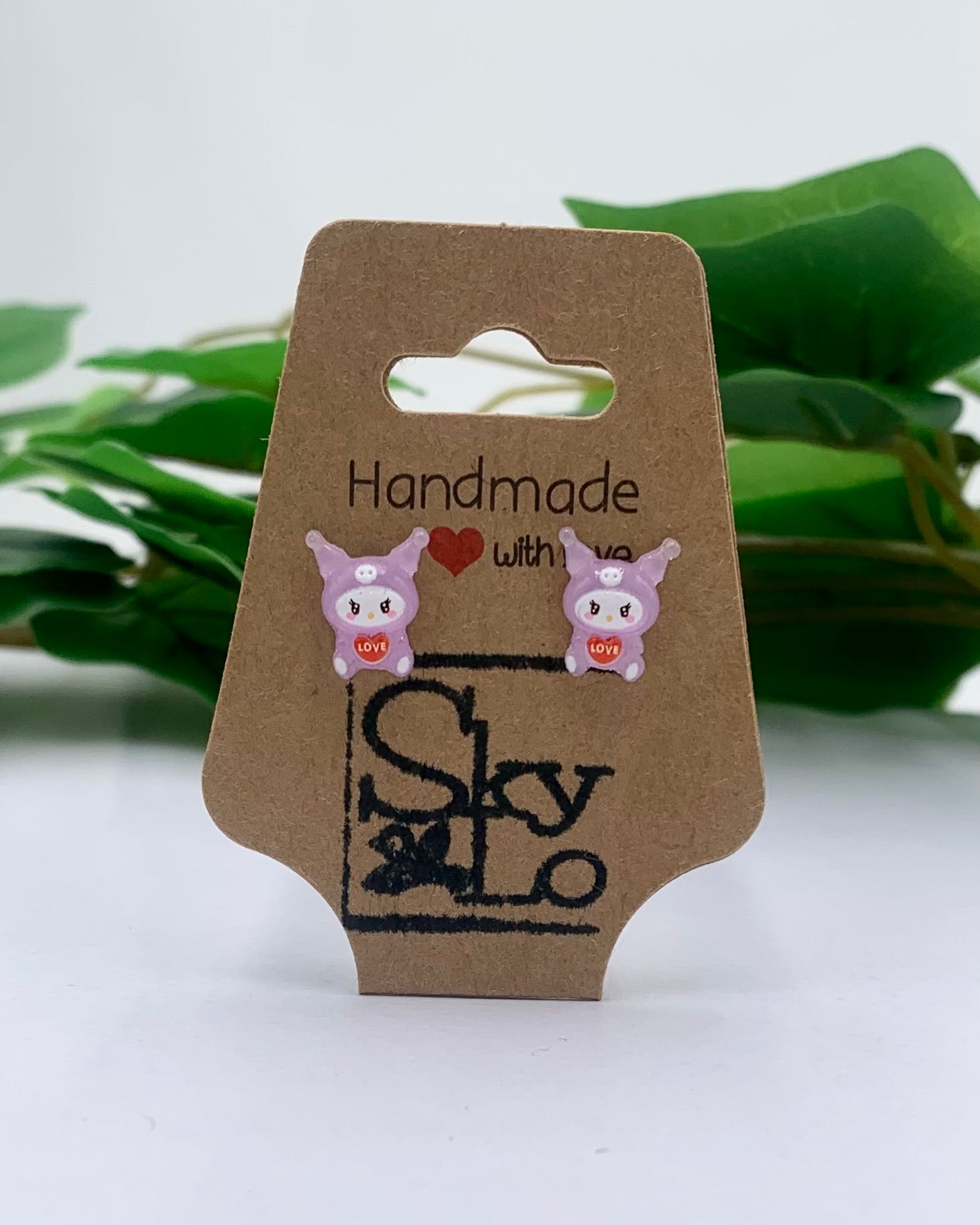 Pair of pink owl-shaped earrings on a 'Handmade with Love' branded card with green leaves in the background.